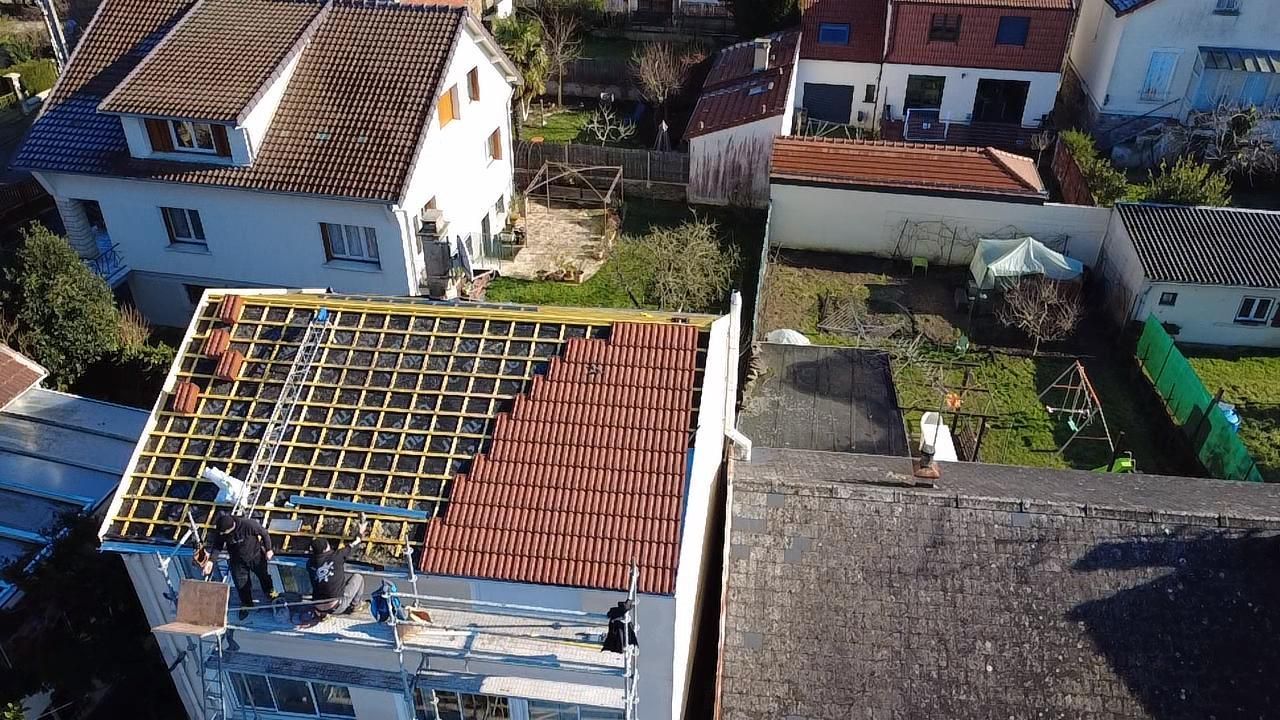 Des ouvriers posent des tuiles sur le toit d'une maison ; toiture partiellement terminée avec des tuiles rouges.