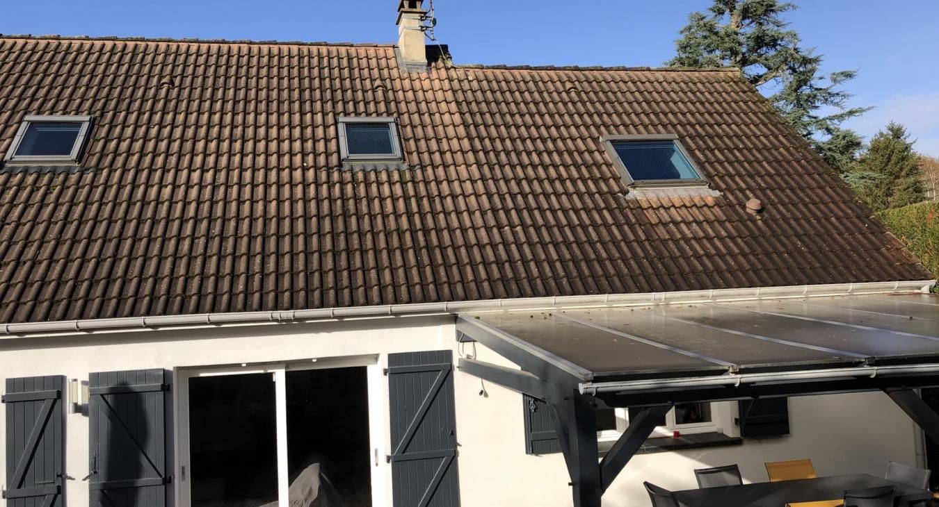 Maison au toit de tuiles brunes, avec trois puits de lumière et un bardage blanc.