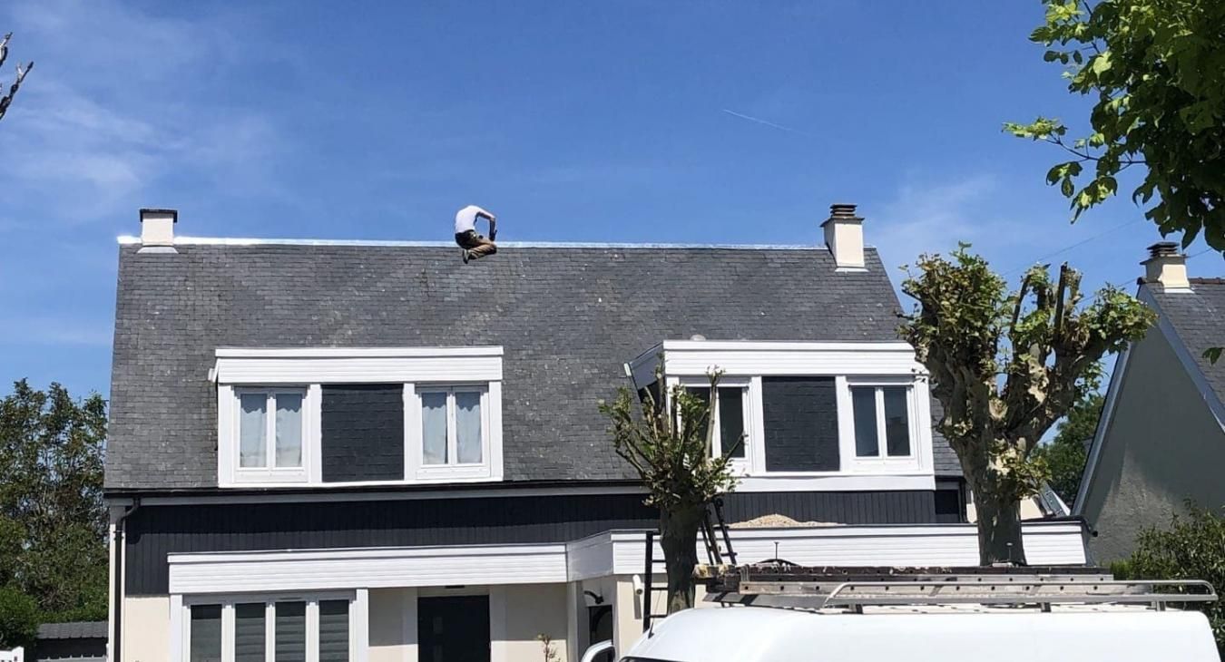 Une personne travaille sur un toit de bardeaux gris sous un ciel d'un bleu éclatant.