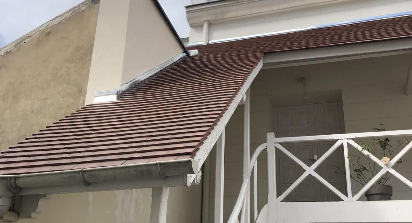 Toit de tuiles brunes d'un bâtiment blanc avec un balcon.