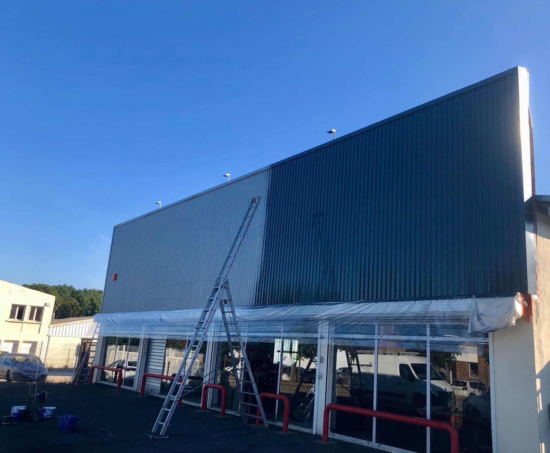 Façade du bâtiment en cours de peinture bleue, avec une échelle. Lumière du soleil.