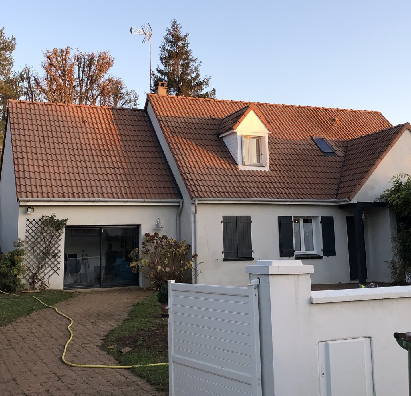 Maison avec toit de tuiles rouges, façade blanche, garage double et allée en briques.