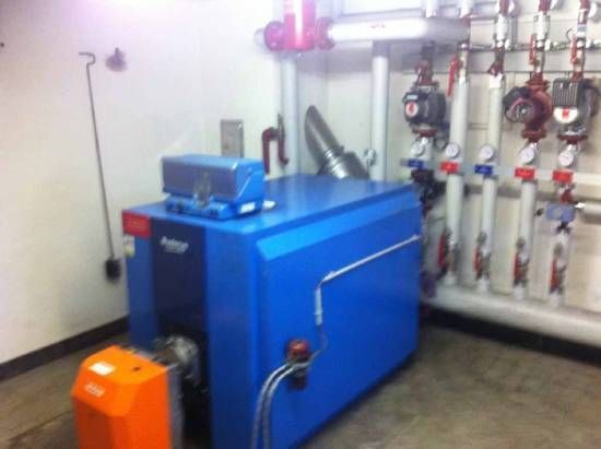 Une chaudière bleue se trouve dans une pièce avec de nombreux tuyaux