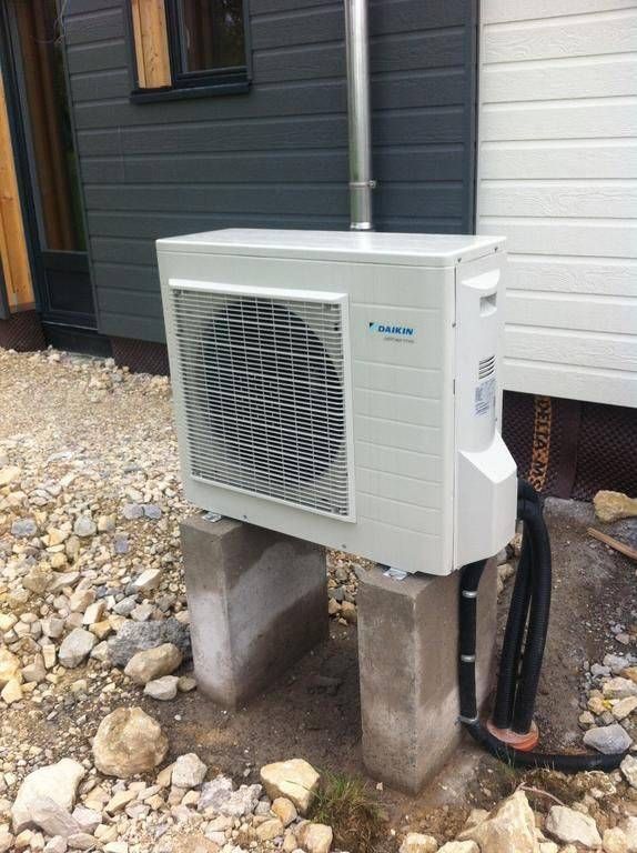 Un climatiseur blanc est posé sur un bloc de béton devant un bâtiment.