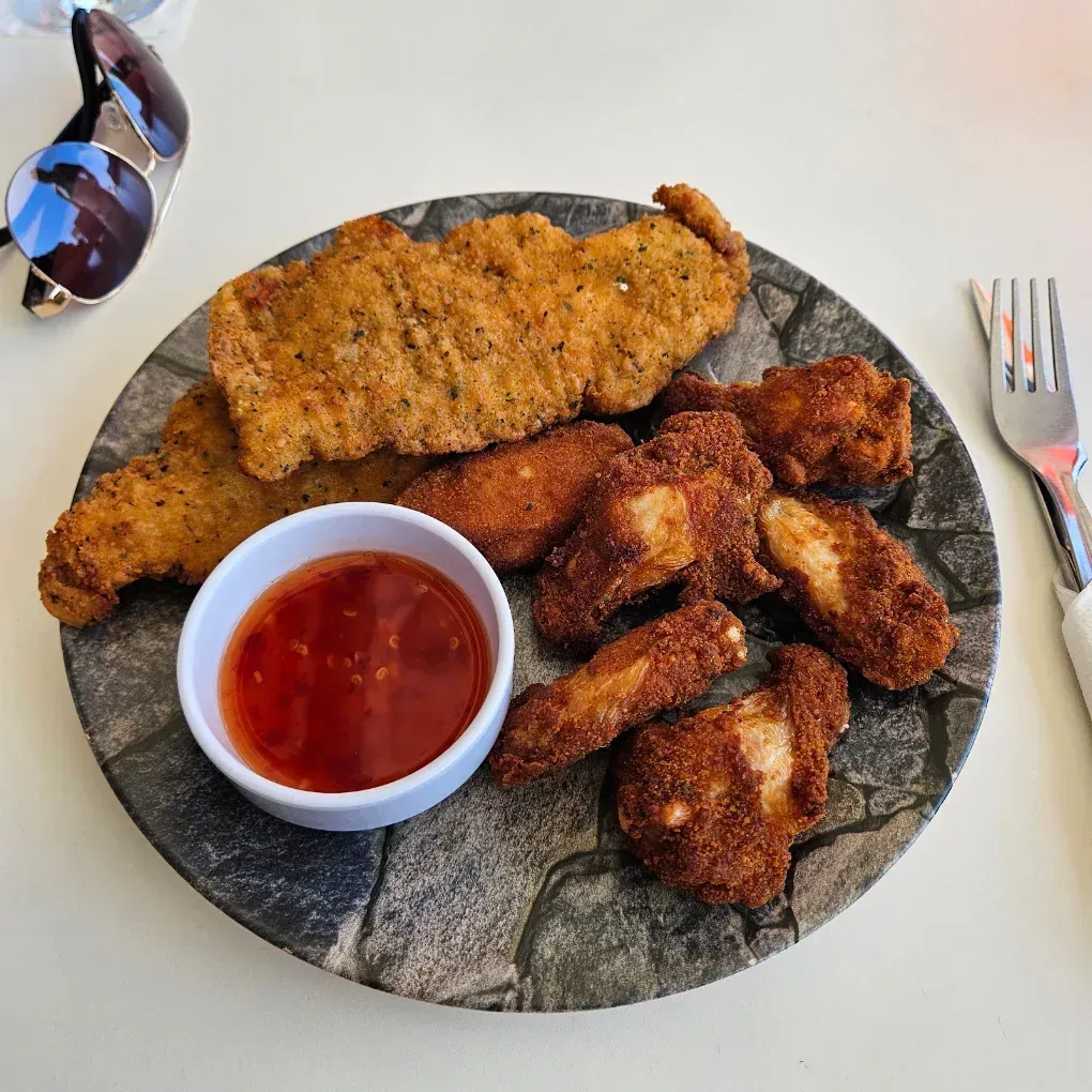 Plato de pollo frito y patatas fritas con salsa roja para mojar sobre una mesa blanca, con gafas de sol cerca.