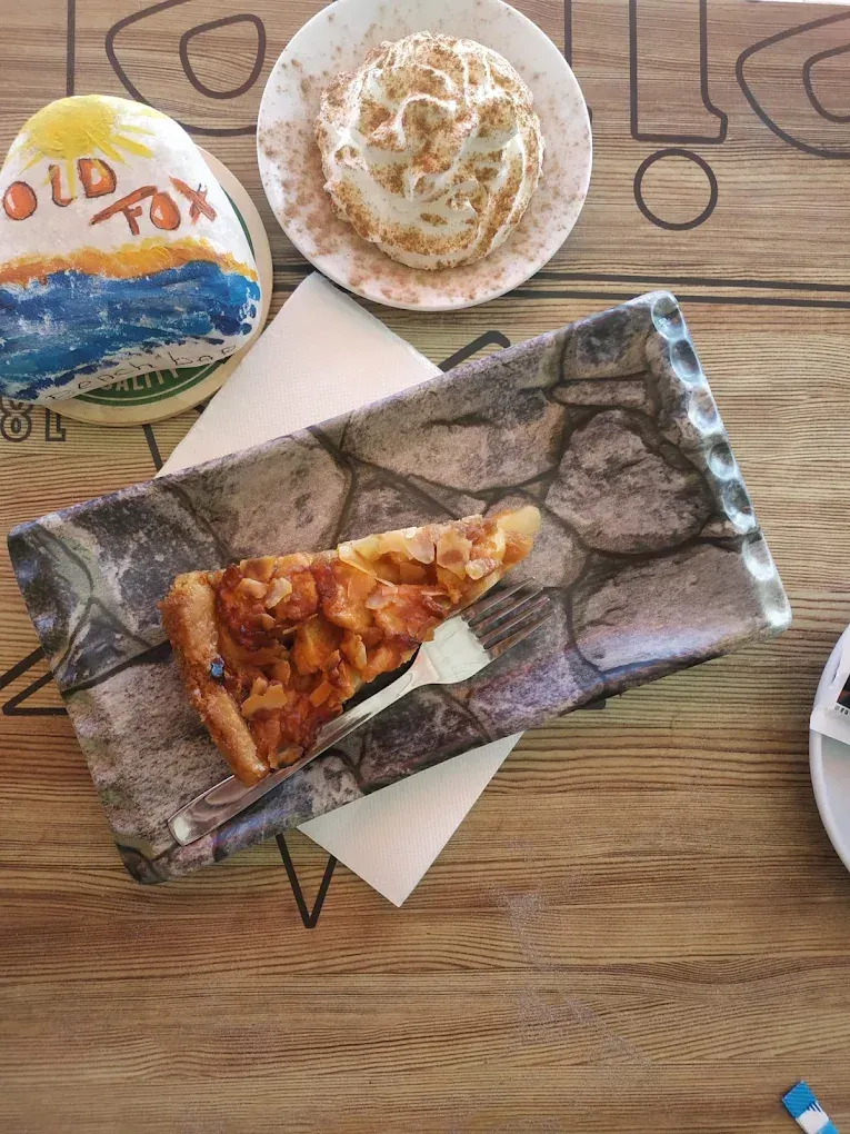 Platos de postre sobre una mesa de madera, que incluyen un pastel glaseado y una porción de pizza en un plato rectangular.