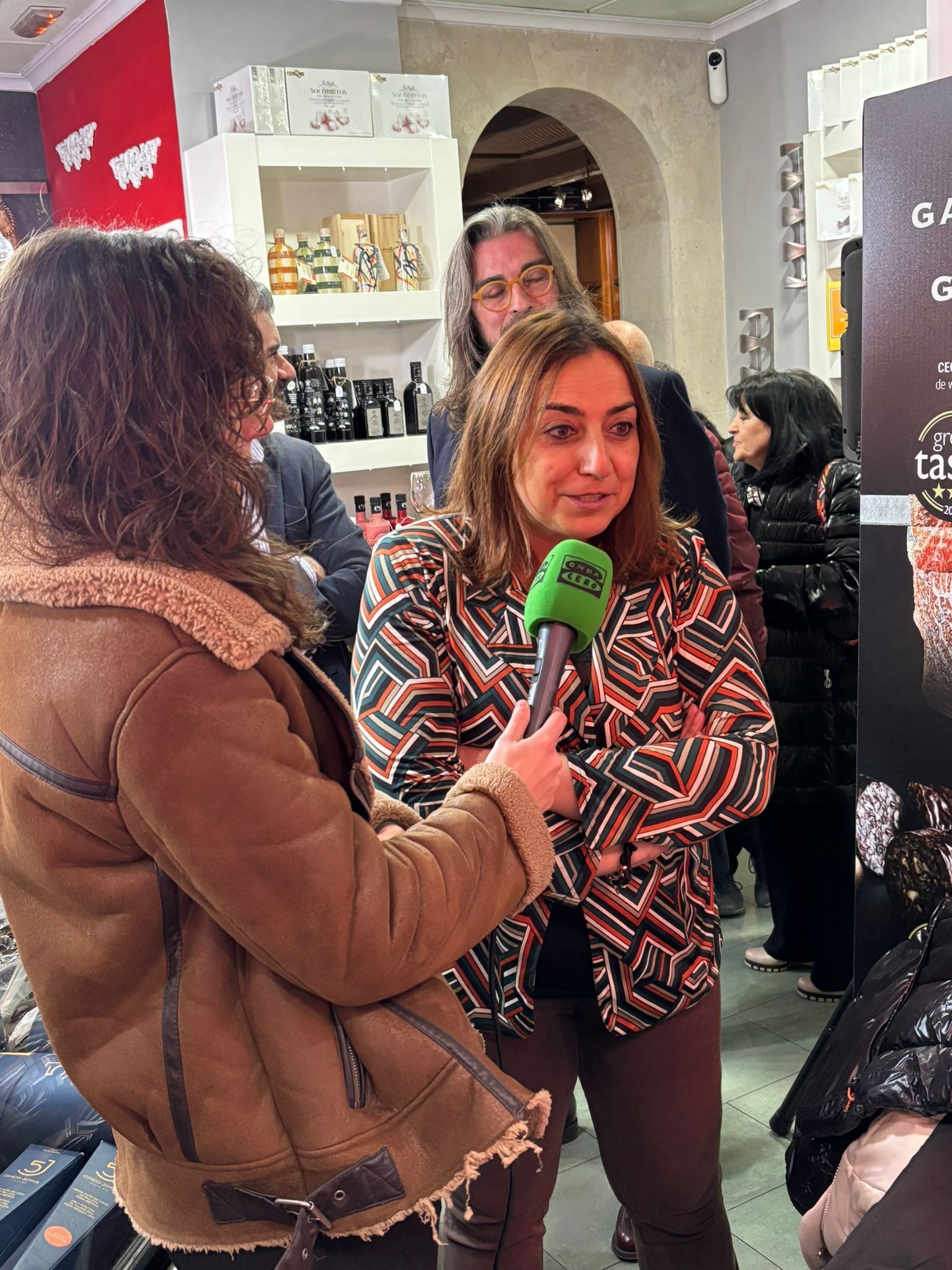 Una mujer está siendo entrevistada en el interior de un local, sosteniendo un micrófono verde
