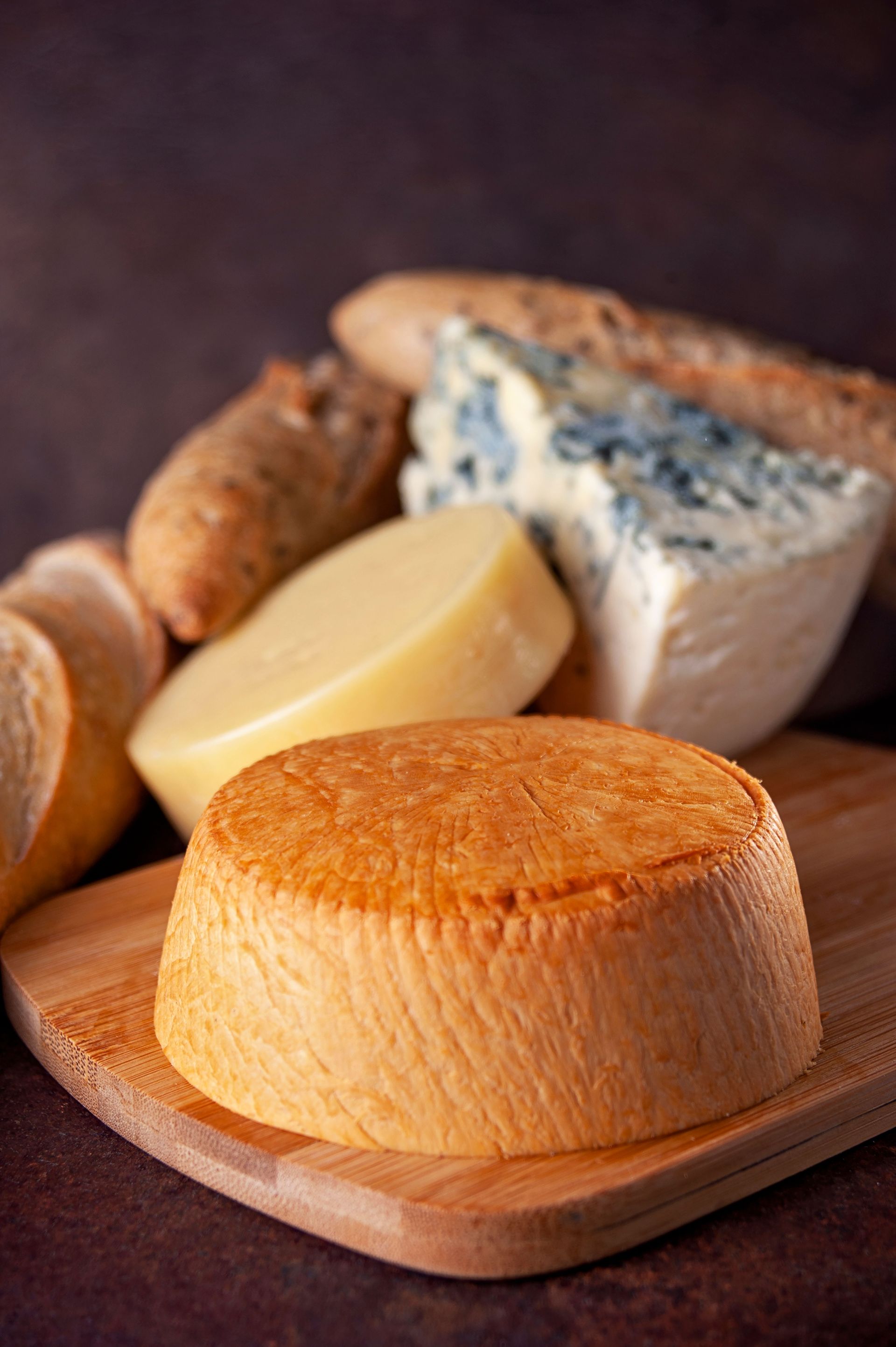 Surtido de quesos en una tabla de madera, incluyendo una cuña de queso azul veteado y un queso redondo de color naranja.