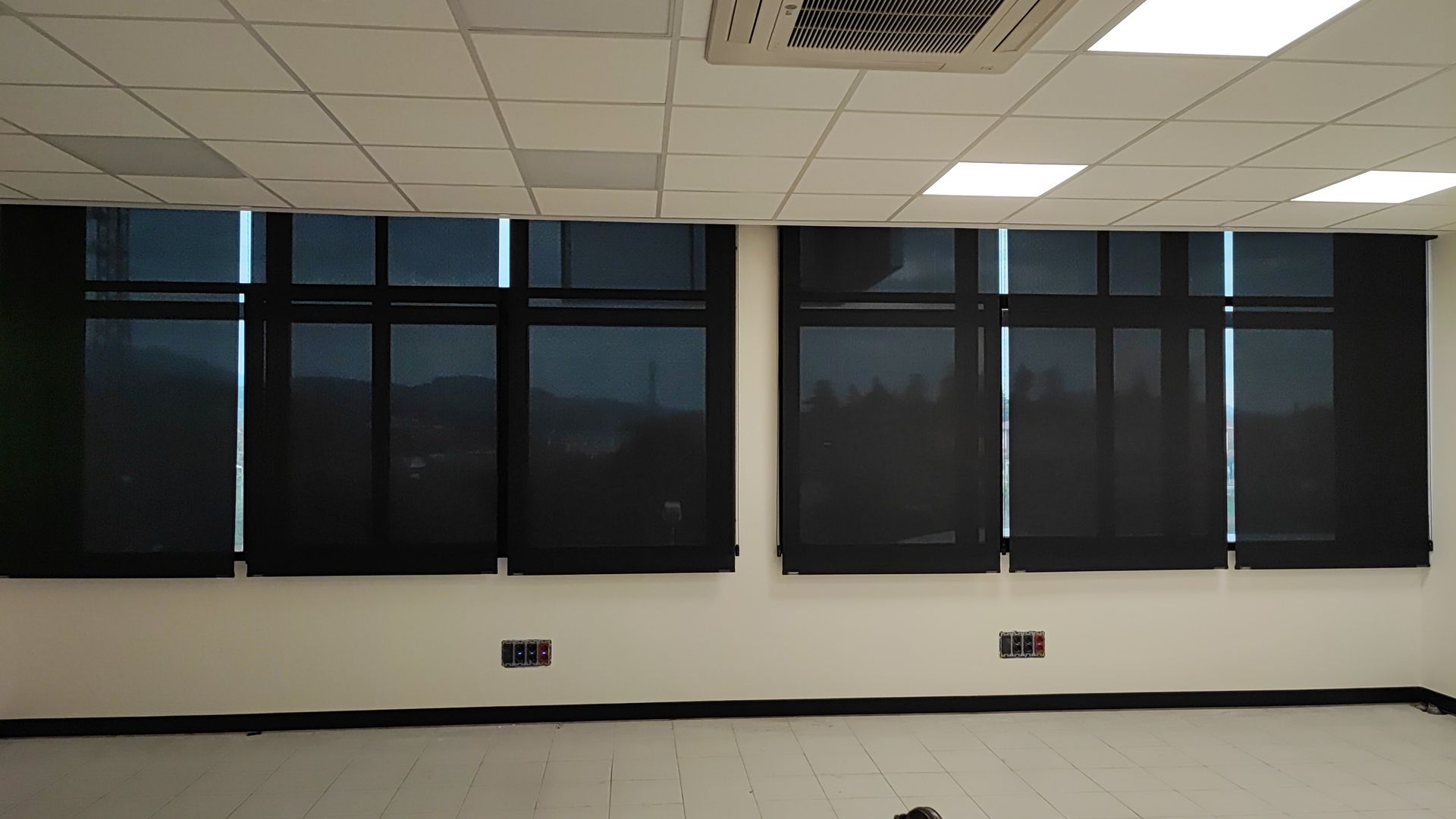 Dos ventanas con cortinas negras dentro de una habitación de paredes blancas y techo suspendido, vistas desde un ángulo bajo.