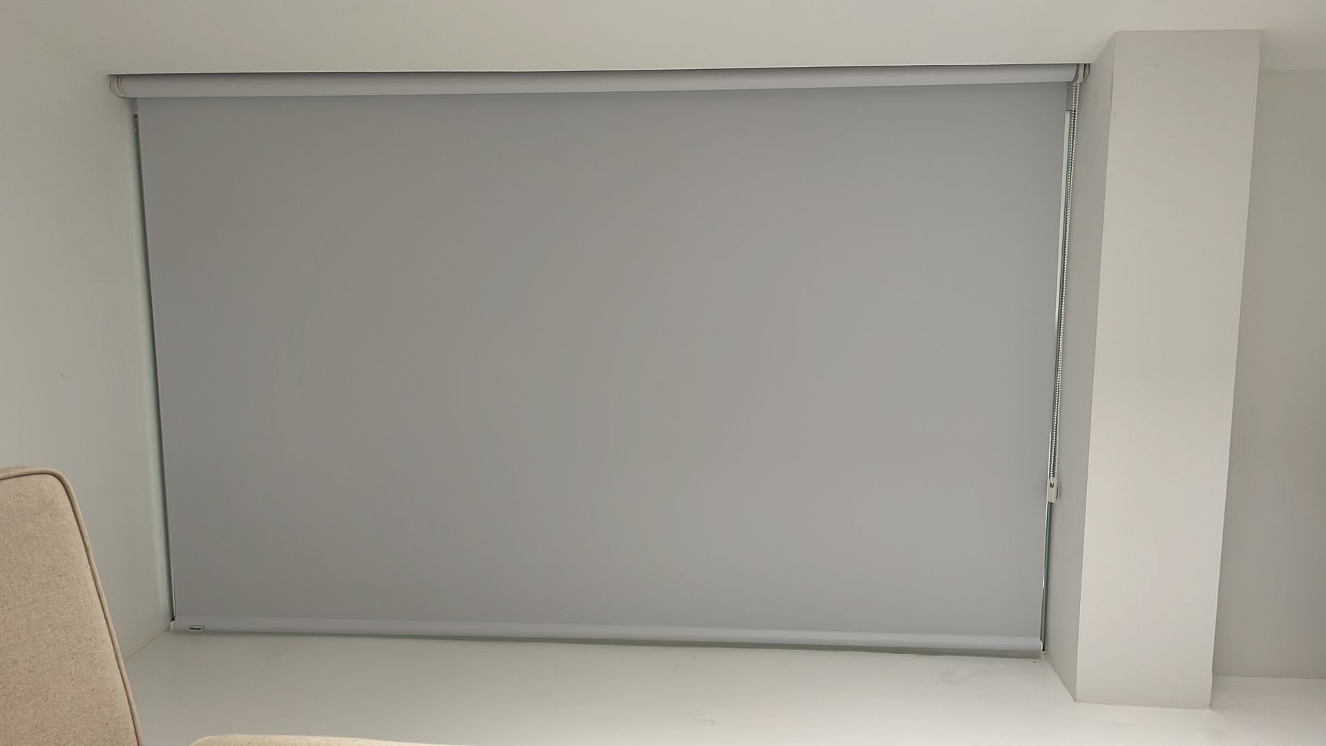 Una gran persiana gris cerrada cubre una ventana. Está instalada en una pared blanca.