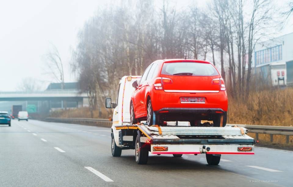 Ein rotes Auto auf einem Abschleppwagen fährt an einem nebligen Tag auf einer Autobahn.