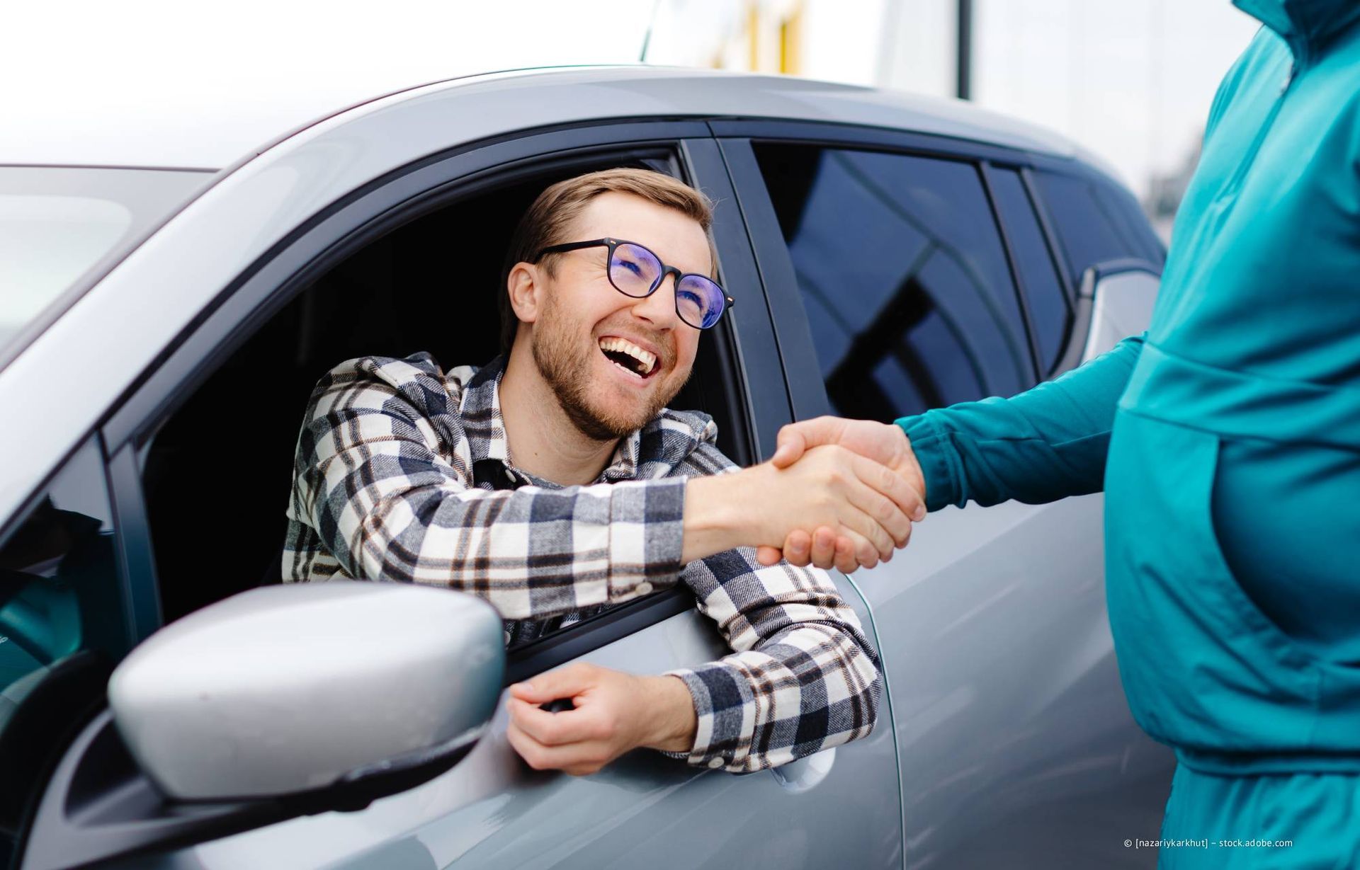 Ein Mann im Auto lächelt und schüttelt einem anderen Menschen die Hand.