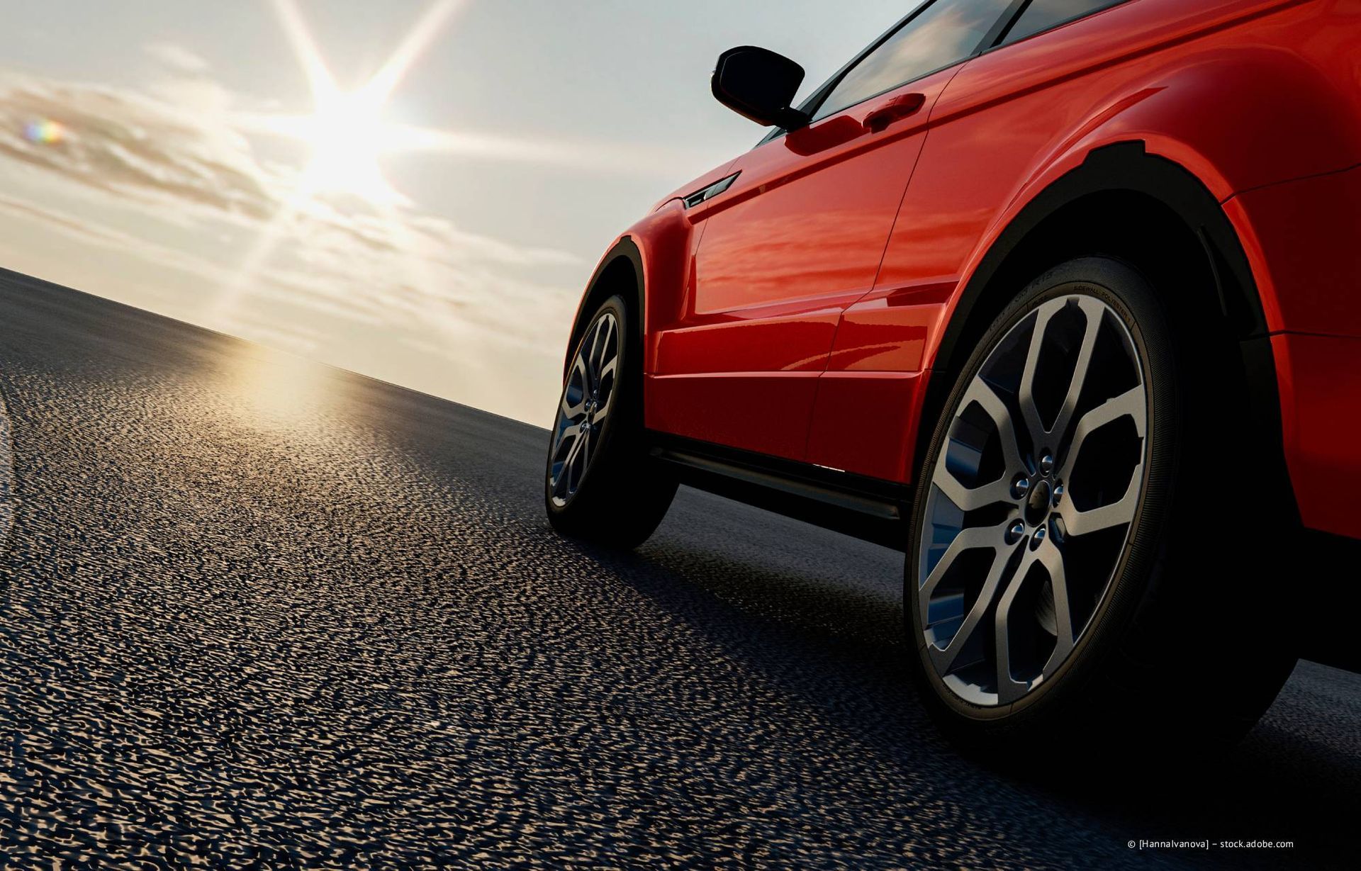 Ein rotes Auto parkt auf Asphalt, im Hintergrund scheint die Sonne.