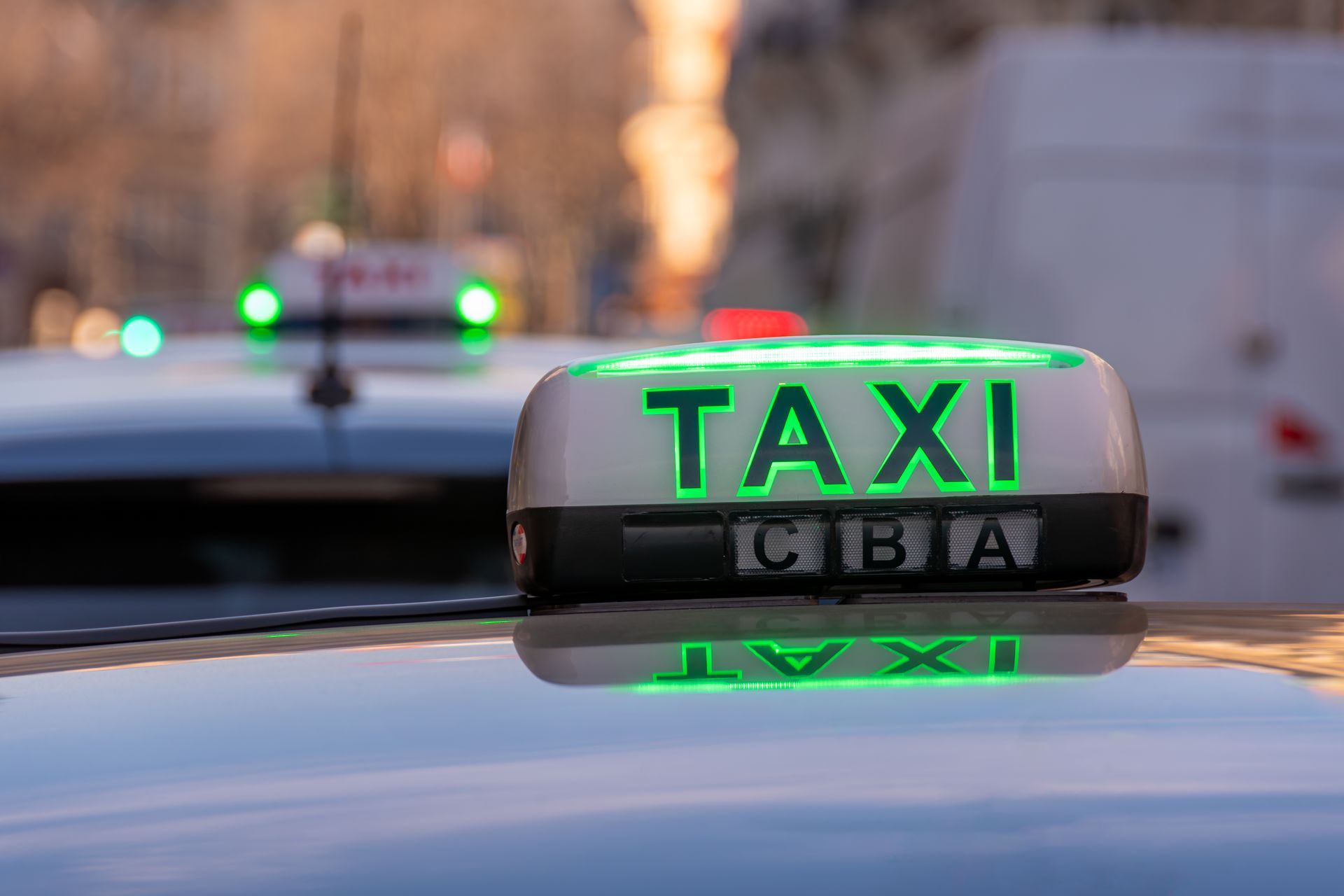 Panneau TAXI gris sur le toit d'une voiture, avec les lumières de la ville floues en arrière-plan.