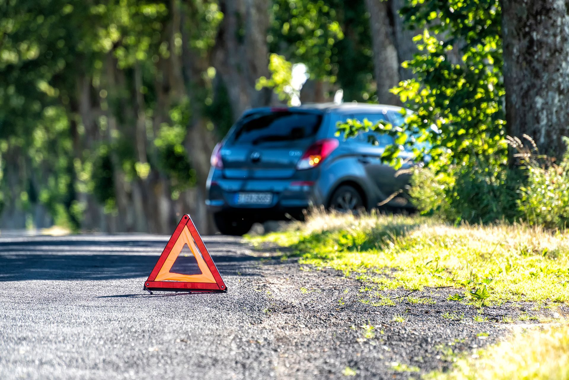 Triangle de signalisation routière au bord d'une route de gravier, avec un SUV bleu garé en arrière-plan.