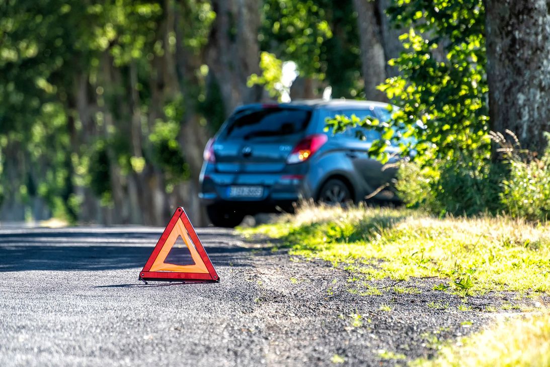 Triangle de signalisation routière au bord d'une route de gravier, avec un SUV bleu garé en arrière-plan.