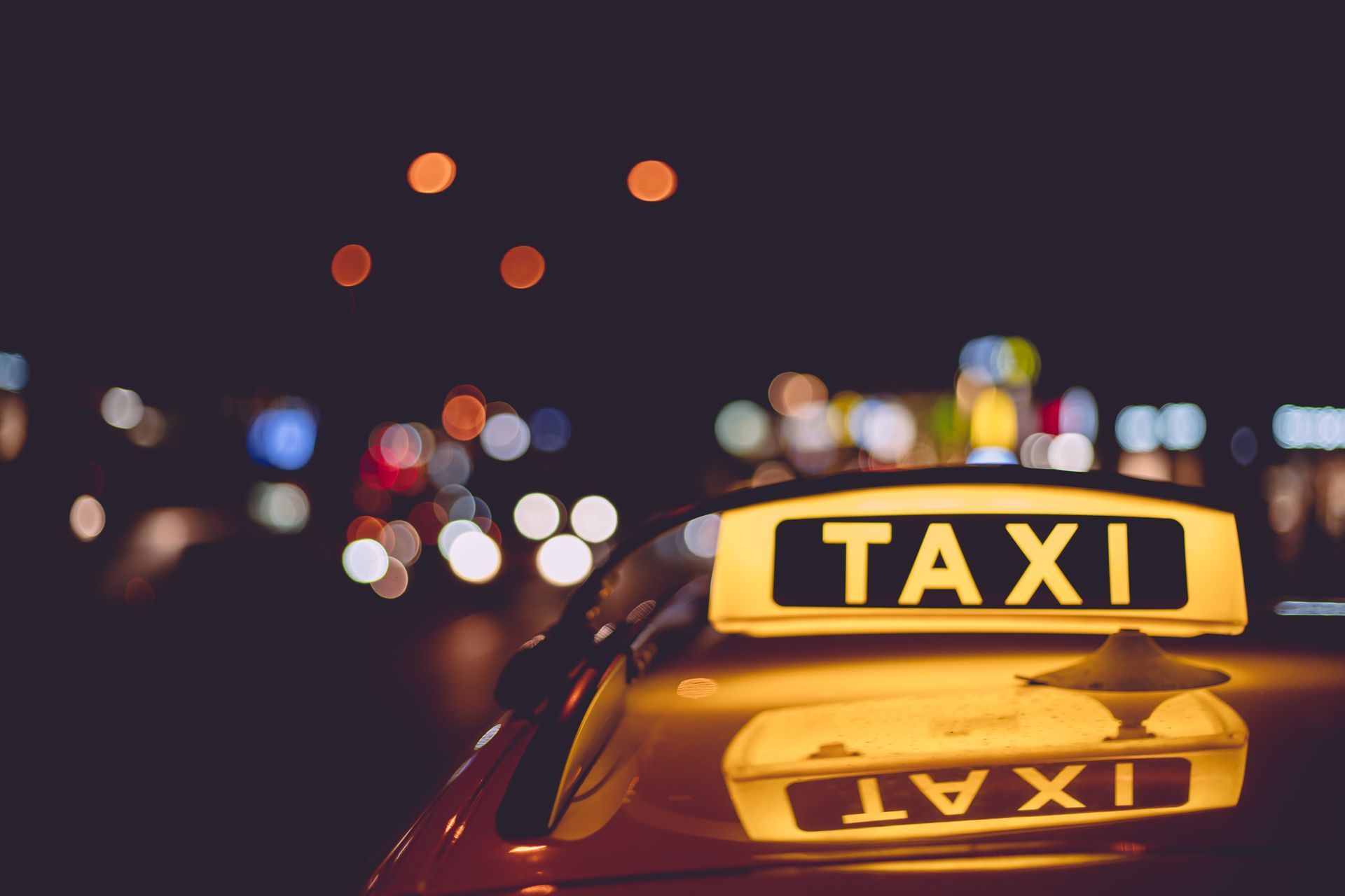 Panneau lumineux de taxi sur le toit d'une voiture, la nuit, avec les lumières de la ville floues en arrière-plan.