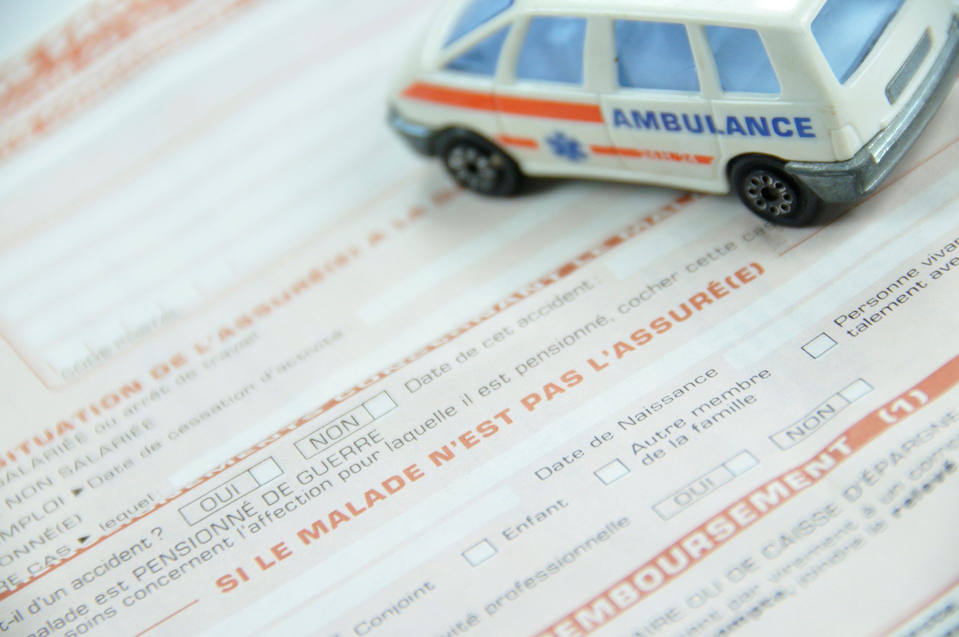 Ambulance miniature sur un formulaire d'assurance maladie français, avec texte orange et noir.
