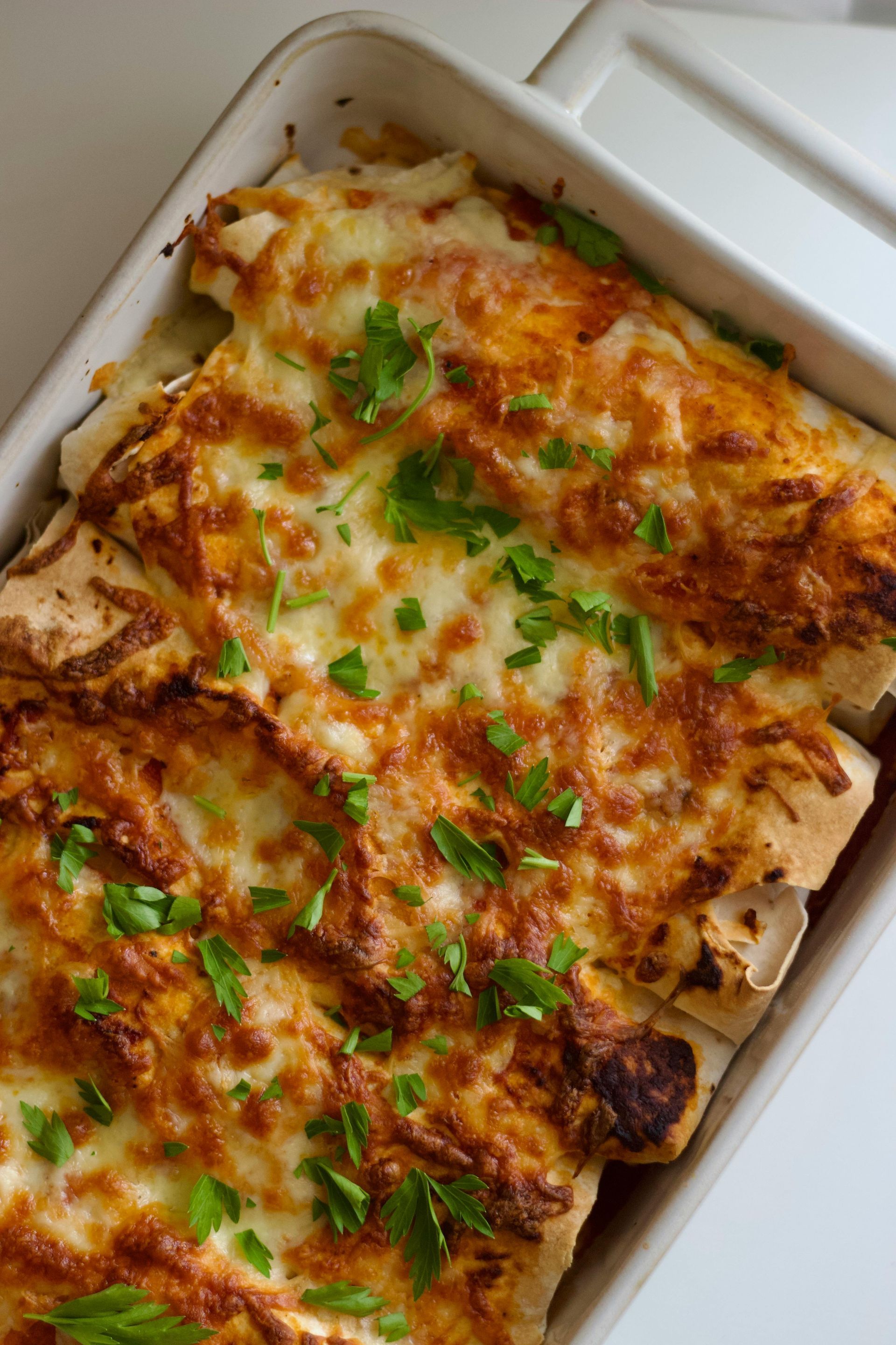 Enchiladas horneadas en un plato blanco, cubiertas con queso fundido y cebolletas picadas.