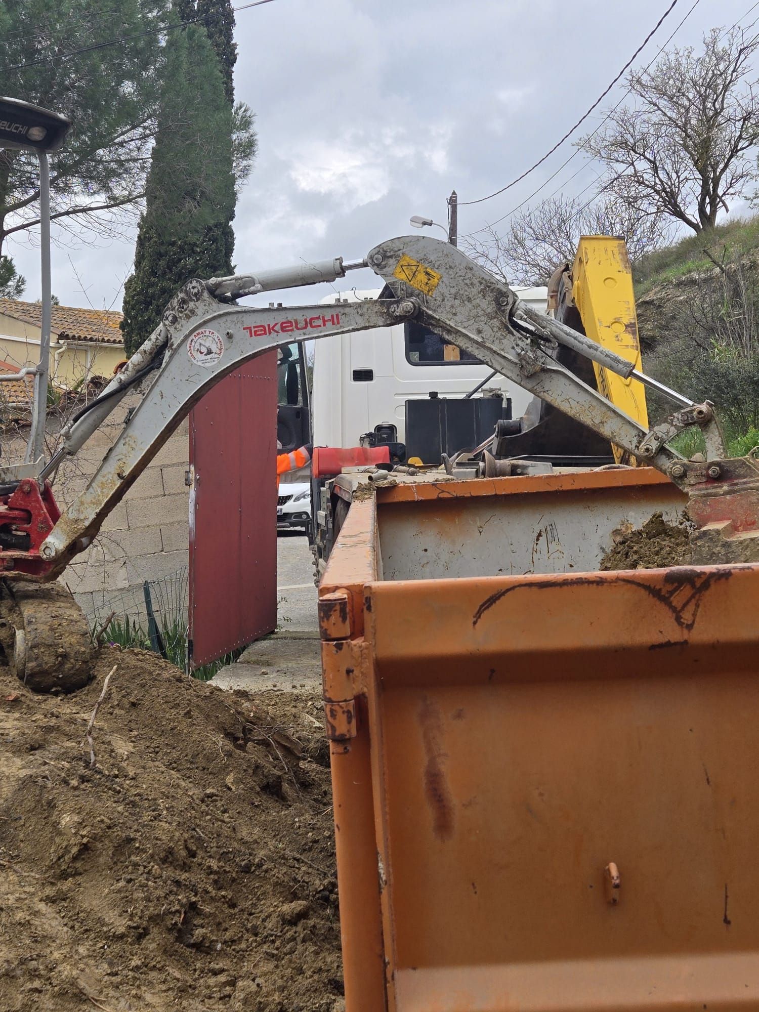 Sur un chantier de construction, le bras d'une excavatrice s'étend au-dessus d'un camion-benne orange.
