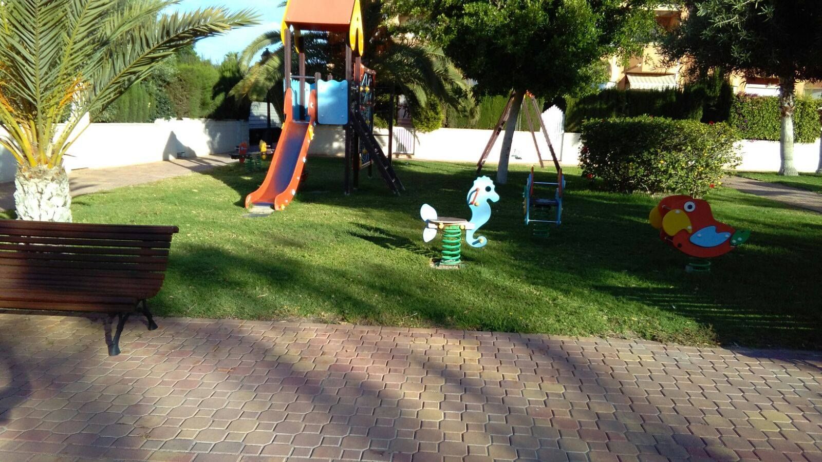 Un parque con un tobogán y columpios y un banco.