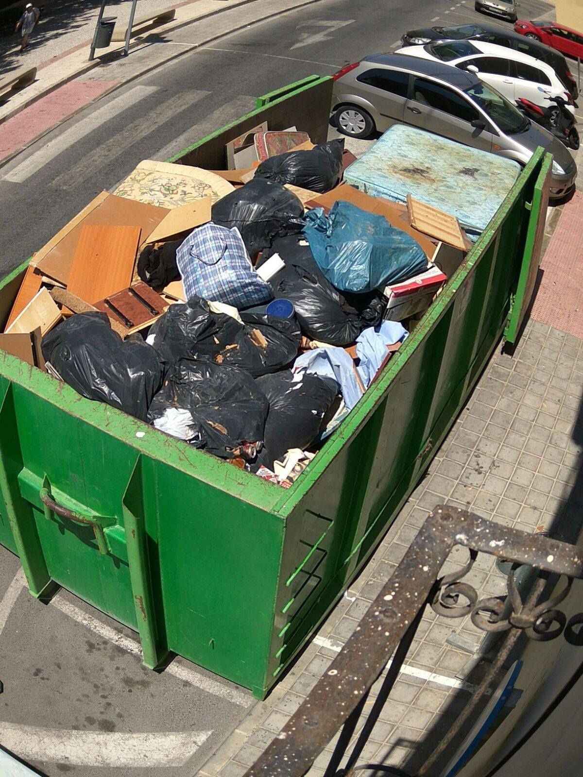 Un contenedor verde lleno de basura se encuentra al costado de la carretera.
