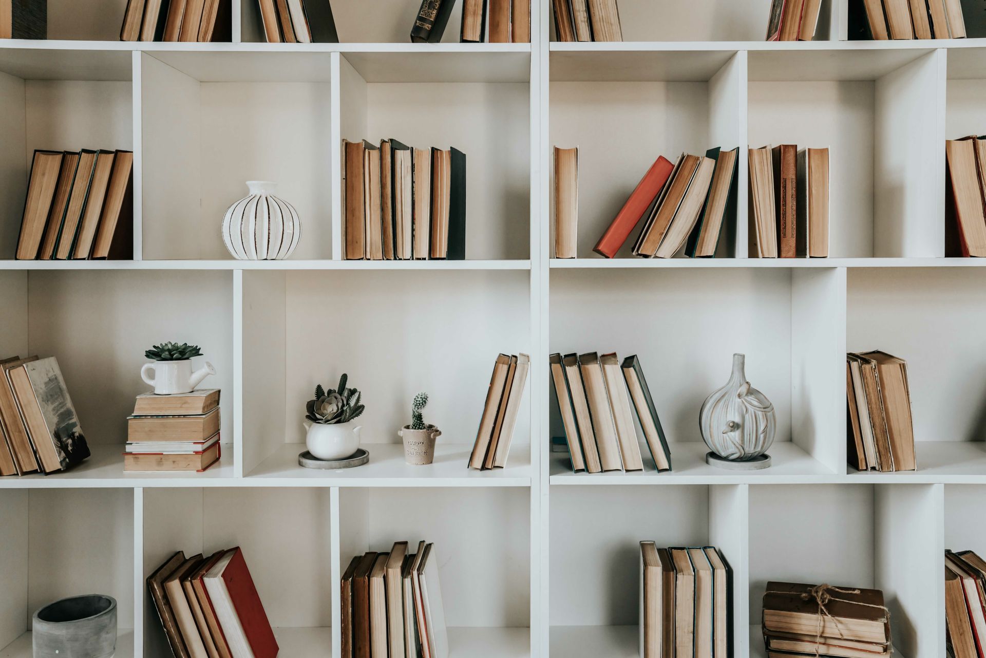 Bibliothèque blanche avec des livres éparpillés, des petites plantes et des objets décoratifs