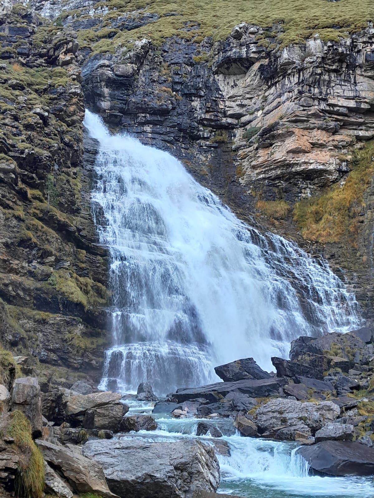 Una cascada está rodeada de rocas y hierba en una ladera.