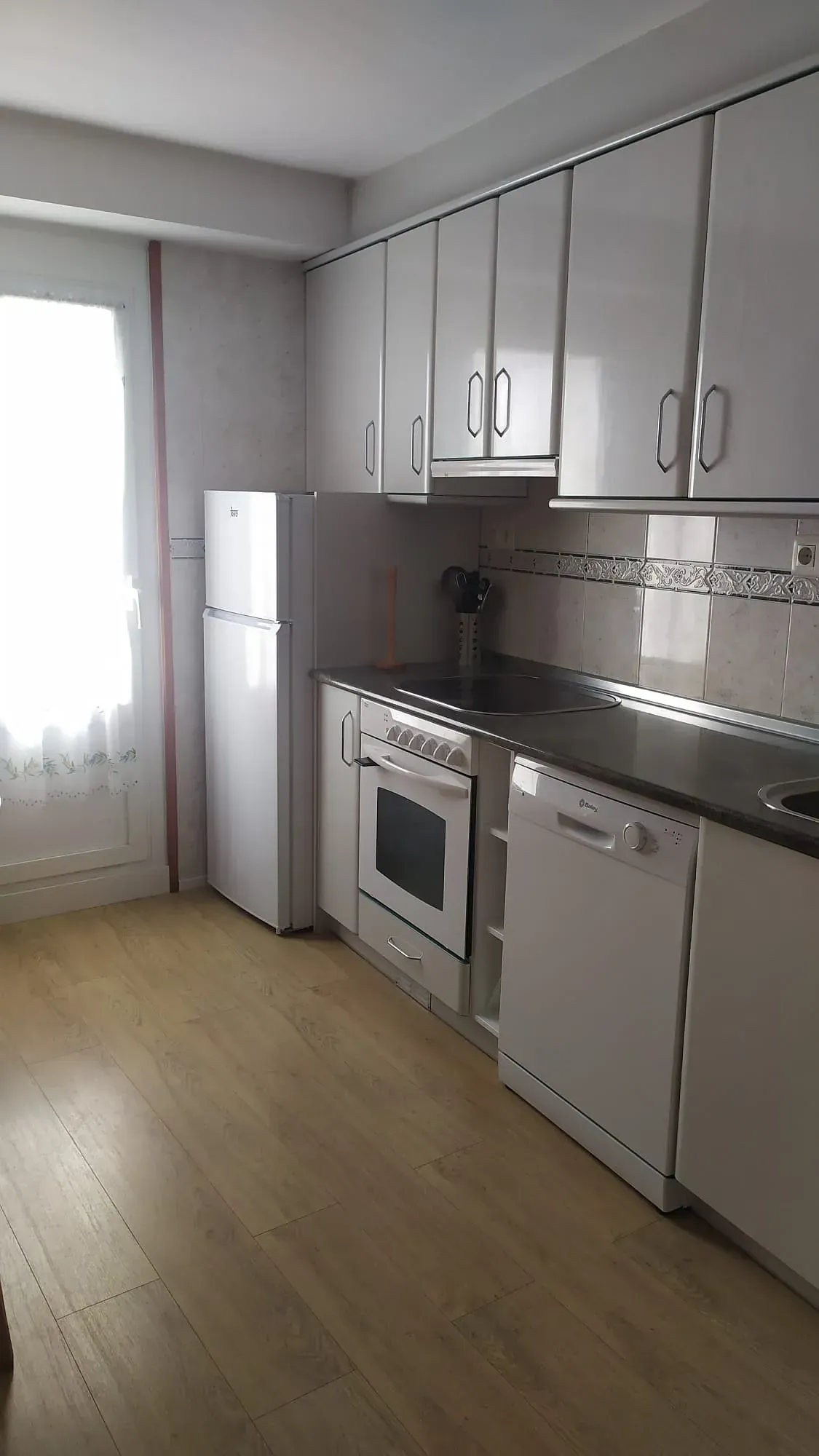 Una cocina con gabinetes blancos, un refrigerador, una estufa y un lavavajillas.