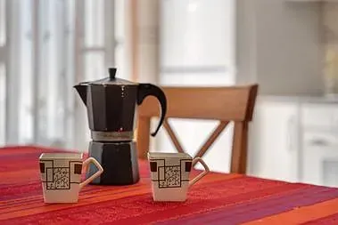 Una cafetera y dos tazas están sobre una mesa.
