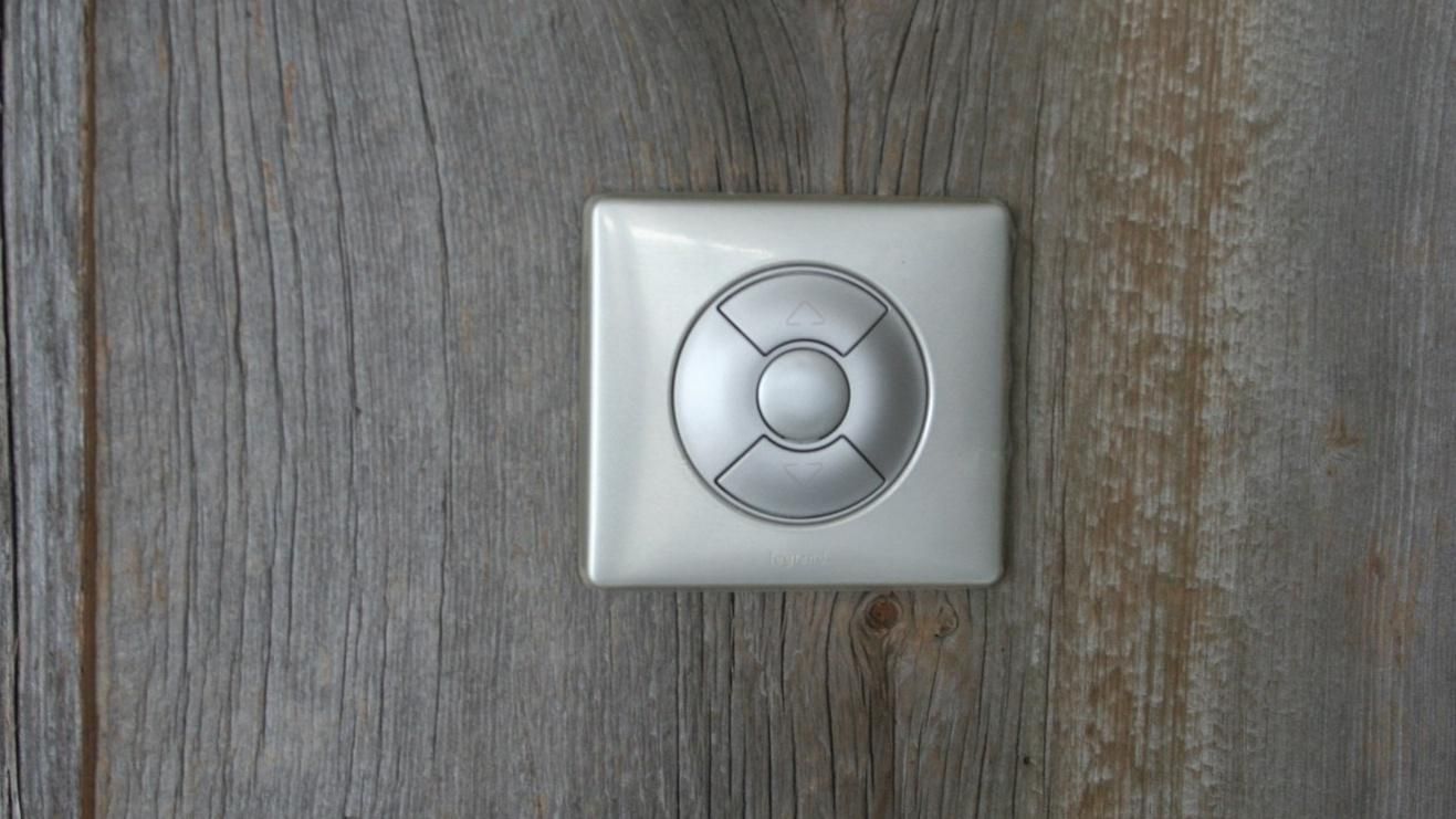 Interrupteur argenté avec boutons directionnels sur un mur en bois.