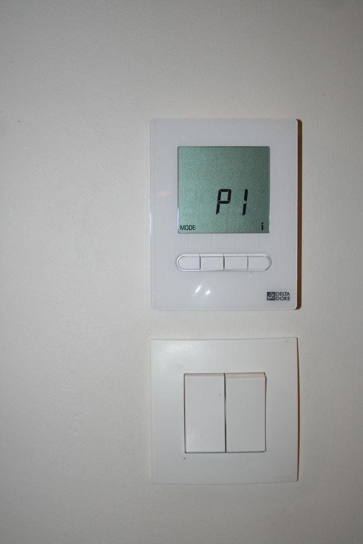Thermostat blanc au-dessus d'un interrupteur à deux boutons sur un mur blanc.