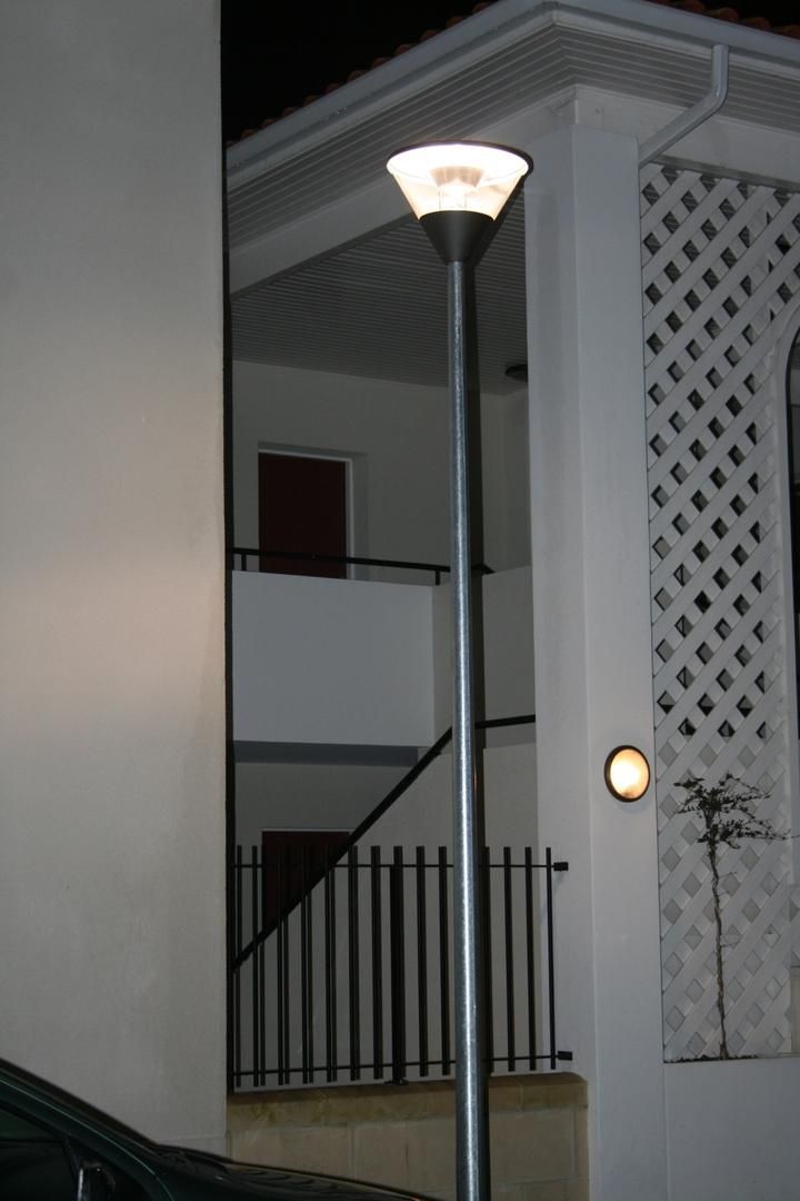 Un lampadaire allumé devant une maison blanche doté d'un escalier et d'une rampe en fer forgé.