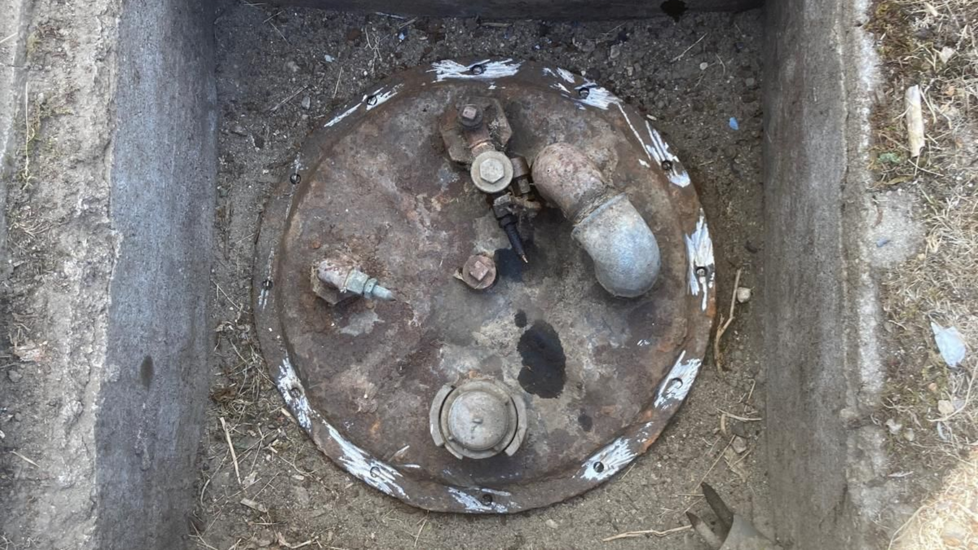 Couvercle de réservoir en métal rouillé avec tuyaux dans un enclos en béton.