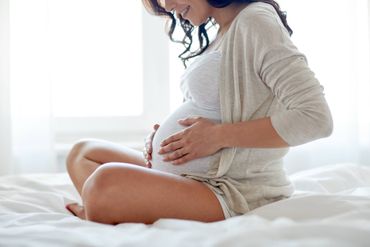 Eine schwangere Frau sitzt auf einem Bett und hält ihren Bauch.