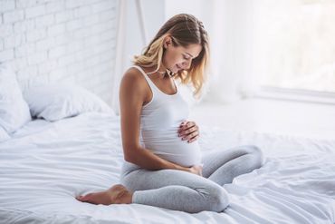 Eine schwangere Frau sitzt auf einem Bett und hält ihren Bauch.
