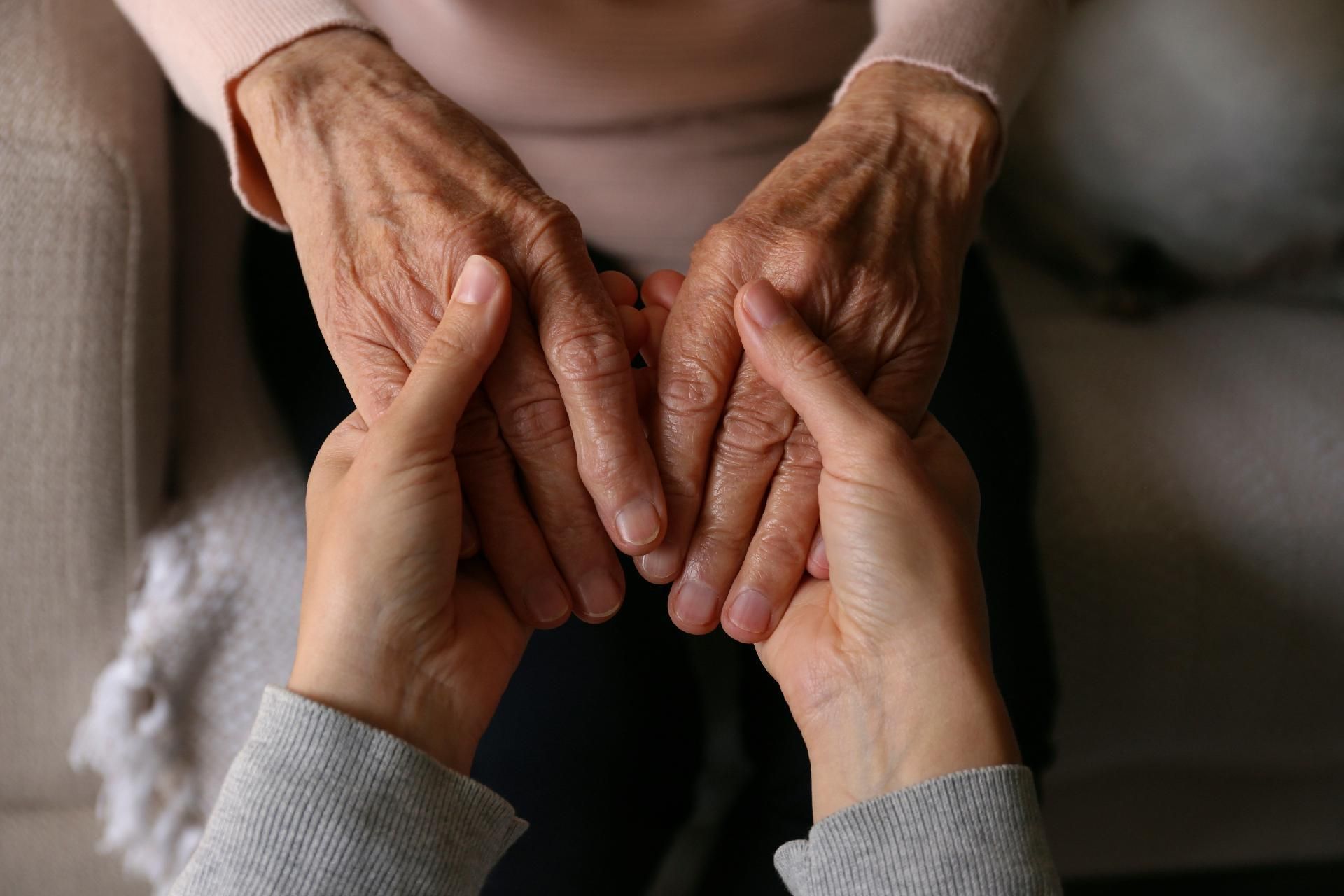 Nahaufnahme von zwei jungen Händen, die sanft die faltigen Hände einer älteren Person halten