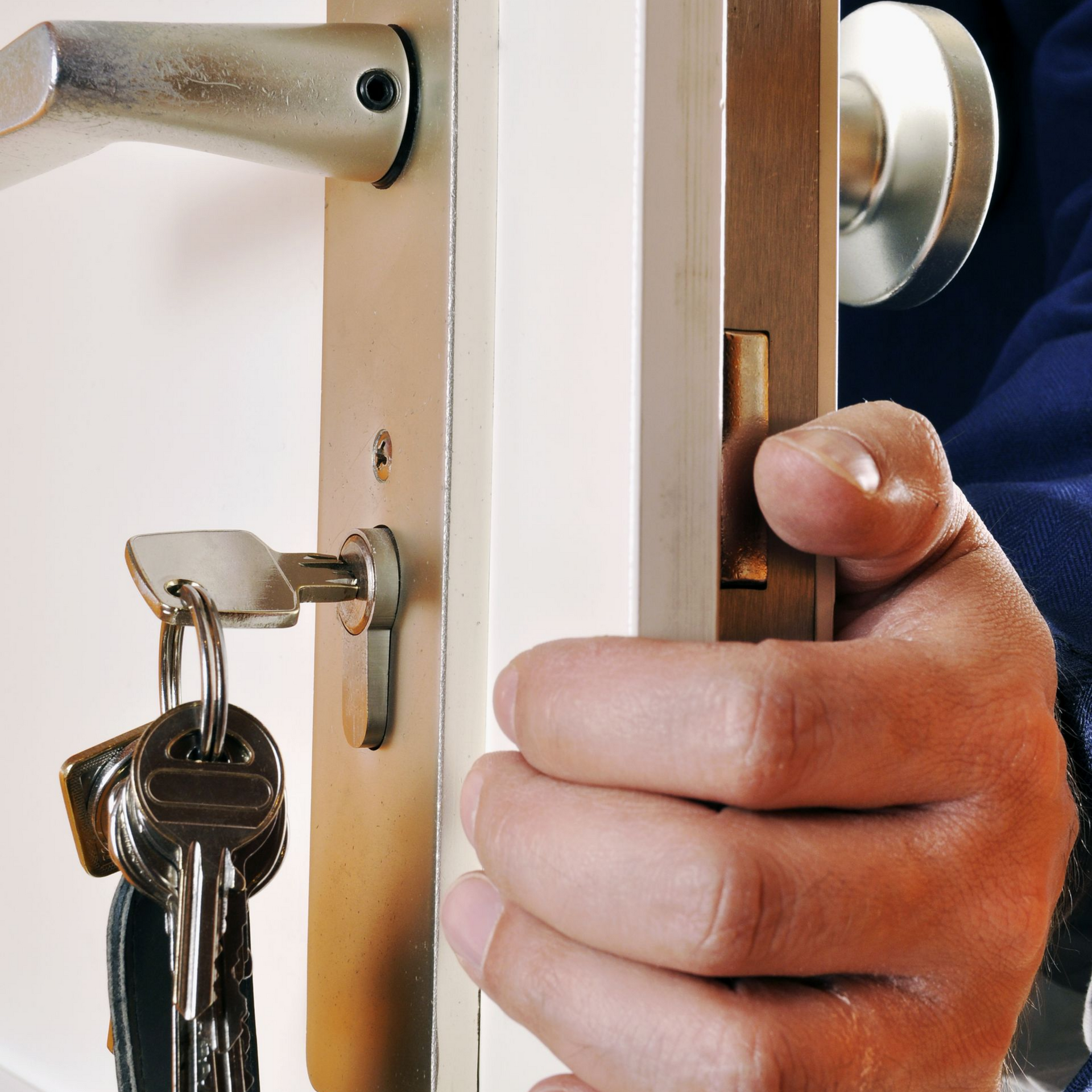 Une main ouvre une porte dont les clés sont dans la serrure. Poignée et serrure en argent ; cadre de porte en bois.