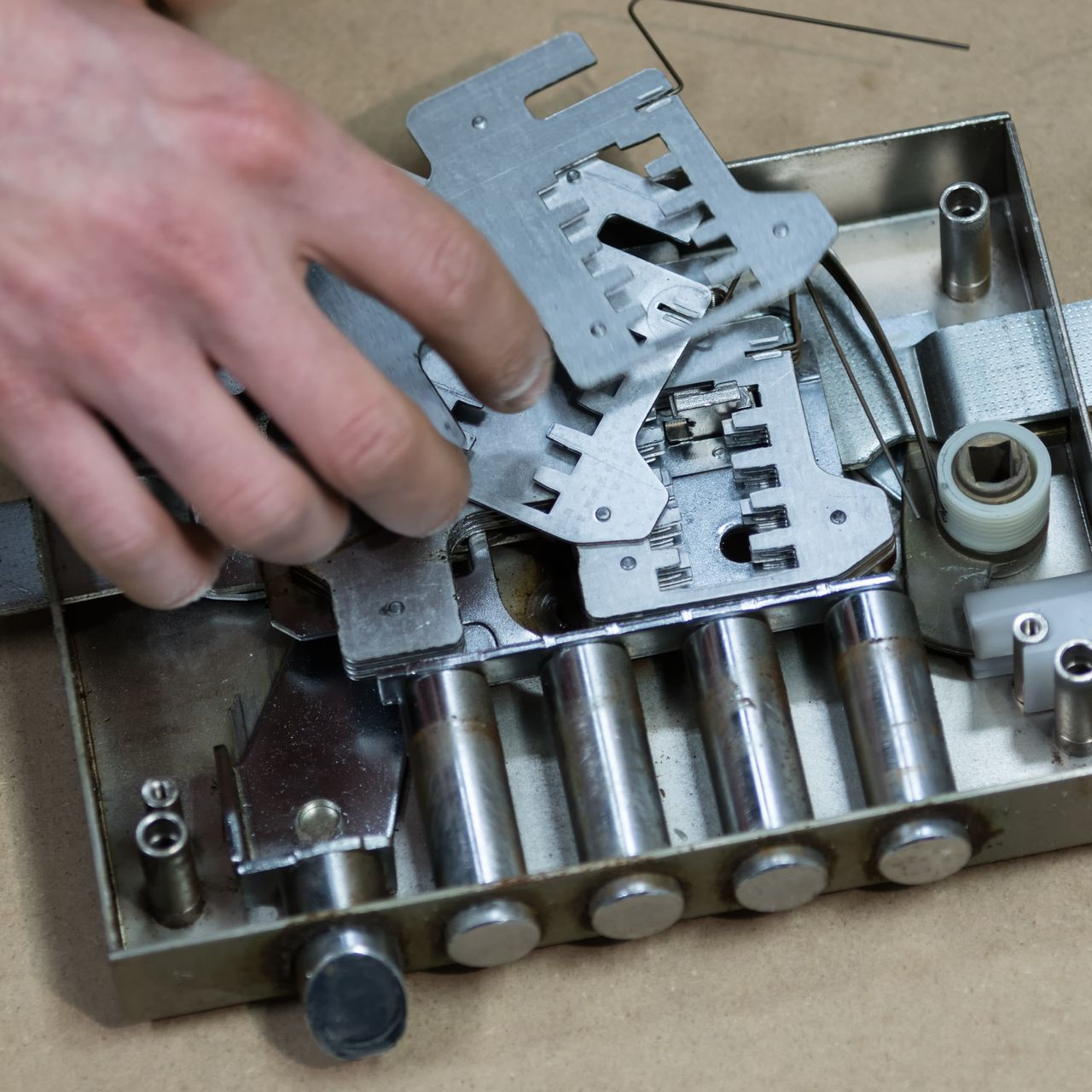 Main d'une personne assemblant un mécanisme de serrure métallique composé de plusieurs éléments et cylindres.