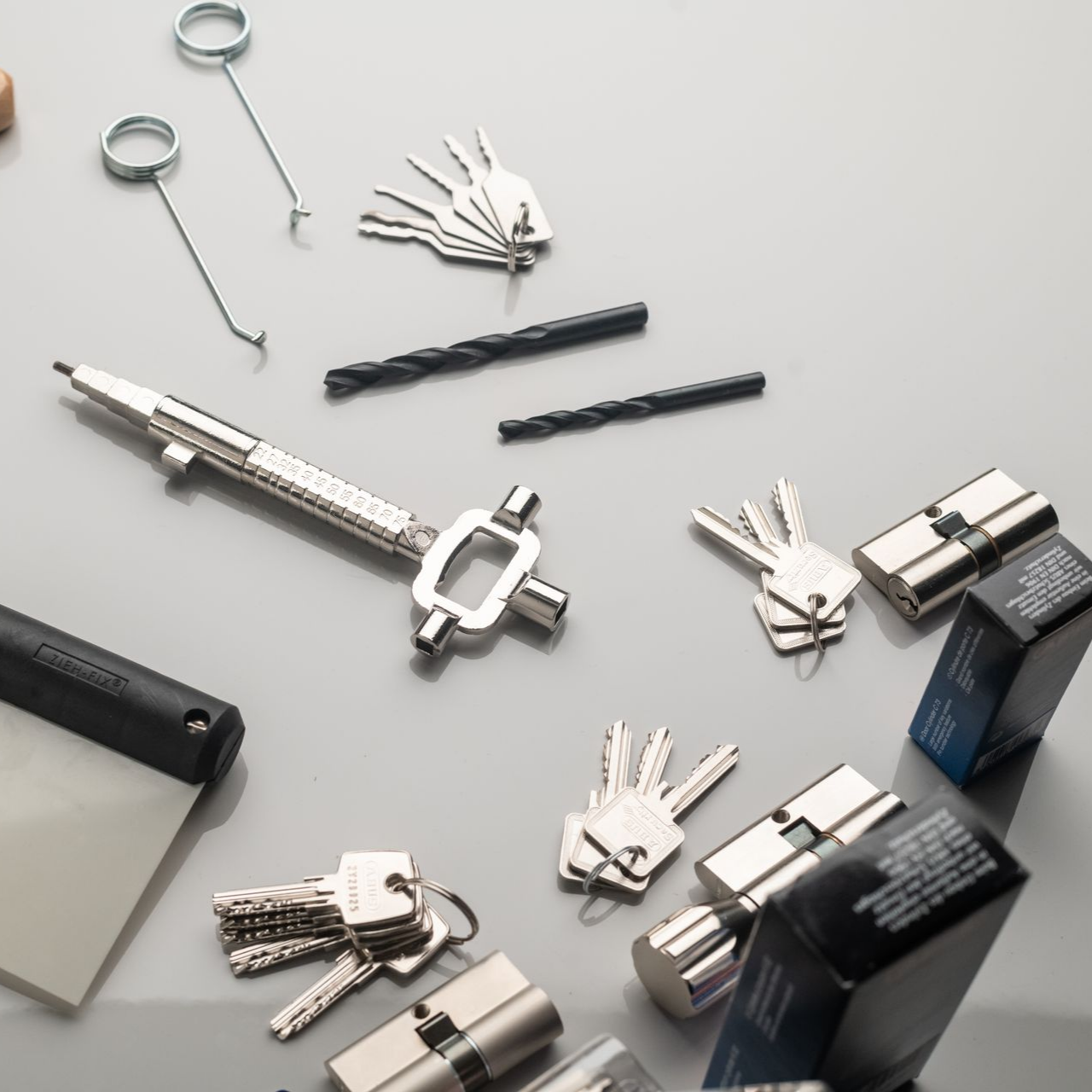 Divers outils de crochetage, clés et cylindres de serrure disposés sur une surface grise.