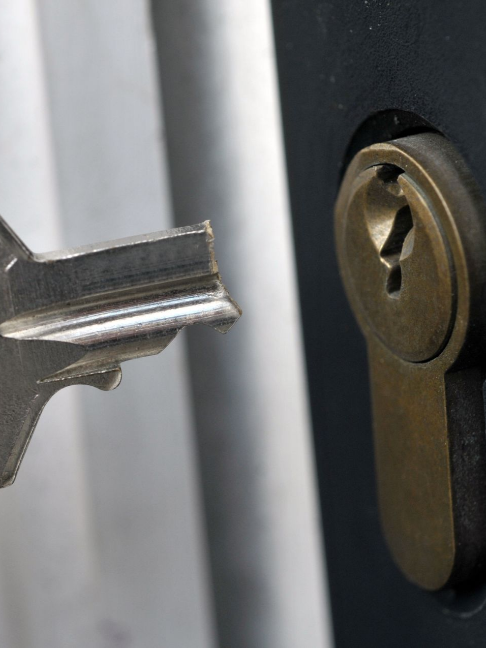 Une clé en argent à côté de la serrure d'une poignée de porte en laiton, sur le point d'être insérée.