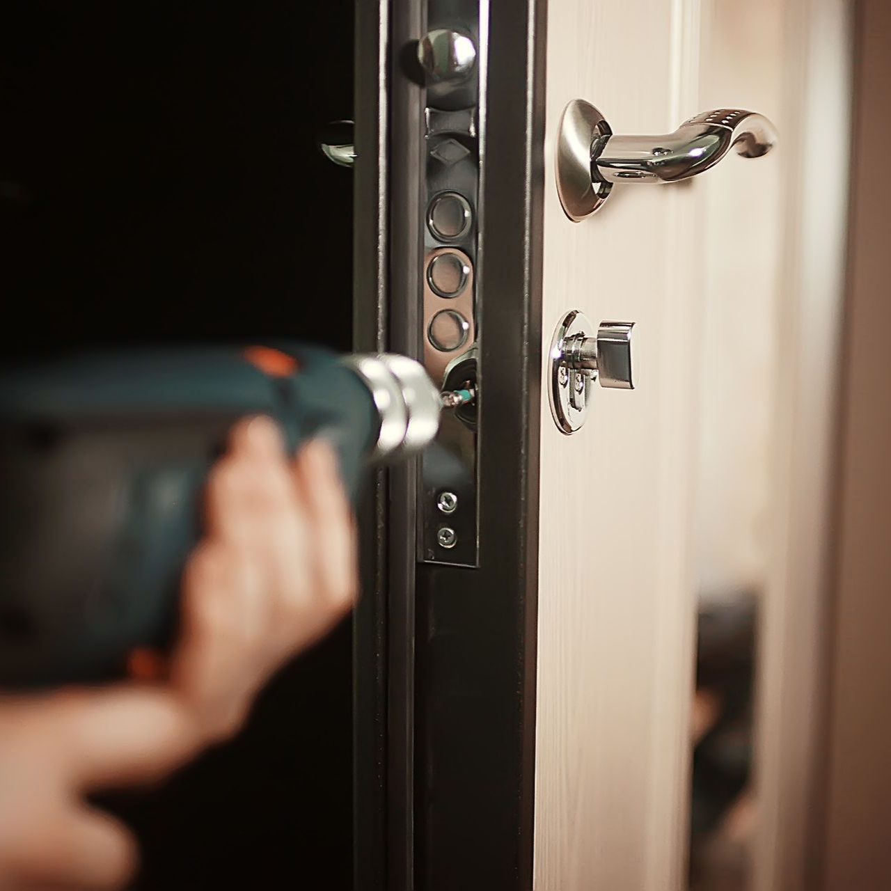 Une personne utilise une perceuse pour installer ou réparer une serrure sur une porte blanche.