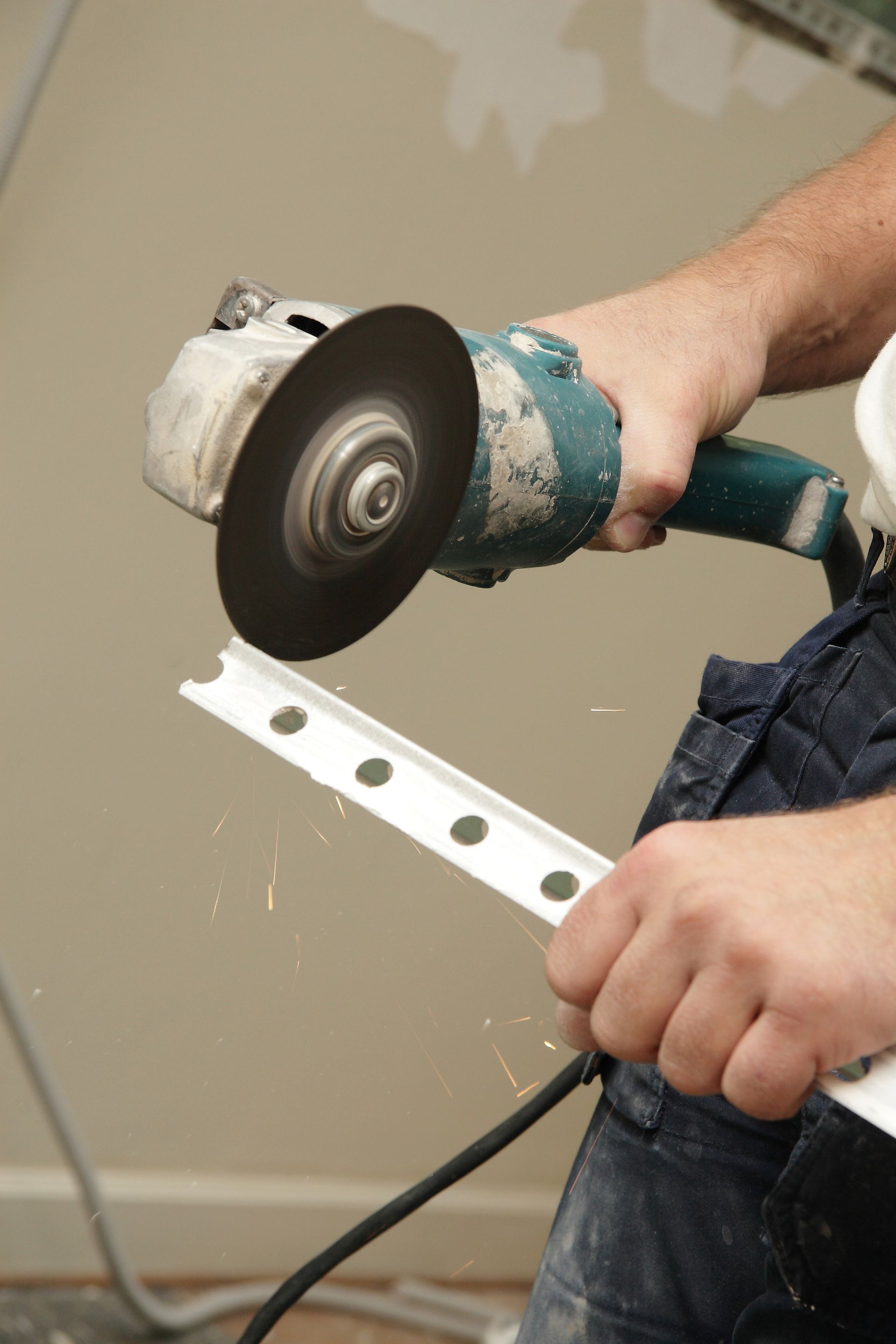 Une personne utilise une meuleuse d'angle pour couper des moulures en plastique blanc à l'intérieur ; des étincelles jaillissent.
