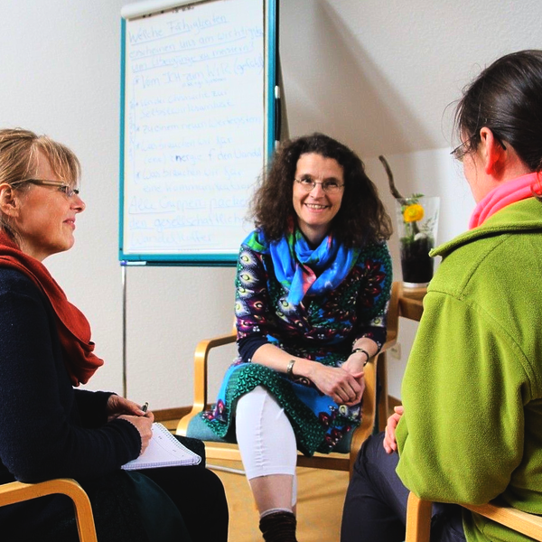 Drei Personen in einer Besprechung, eine lächelt in die Kamera, im Hintergrund ein Flipchart.