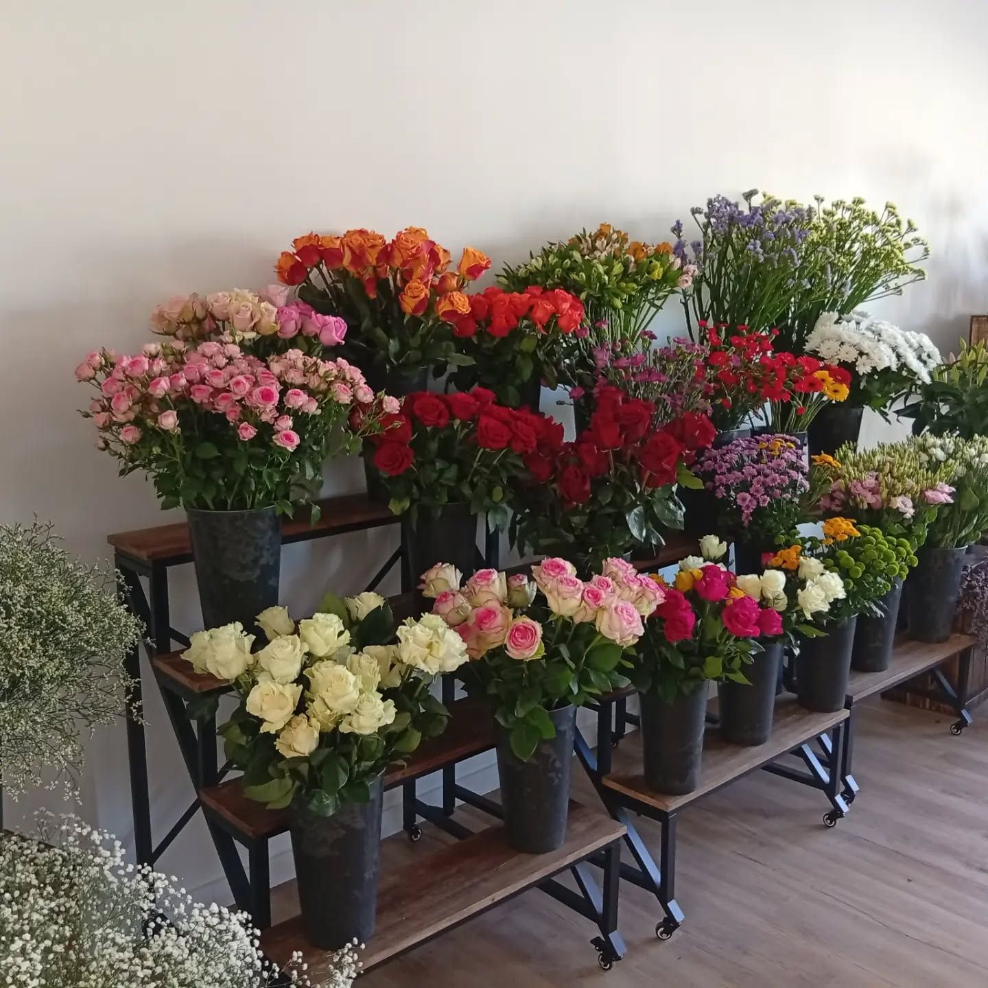 Des rangées de fleurs colorées en pot présentées sur des chariots en bois à plusieurs niveaux dans un magasin.