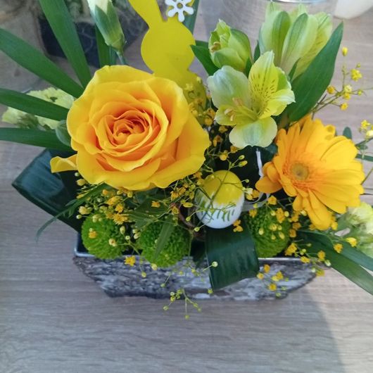 Bouquet de roses jaunes et de gerberas avec des lys blancs dans un récipient gris sur une table.
