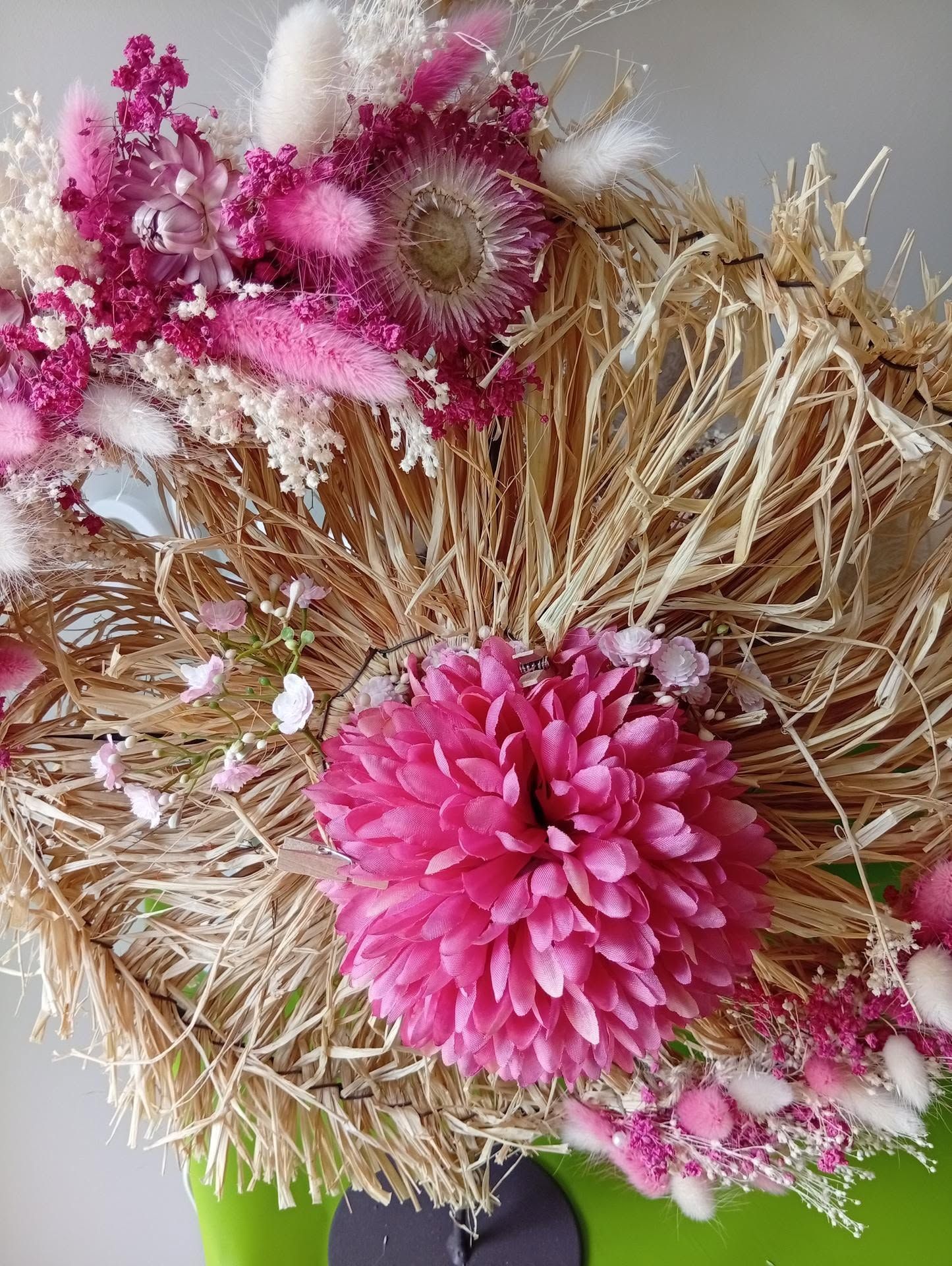 Des fleurs séchées roses et blanches disposées dans une couronne de paille.