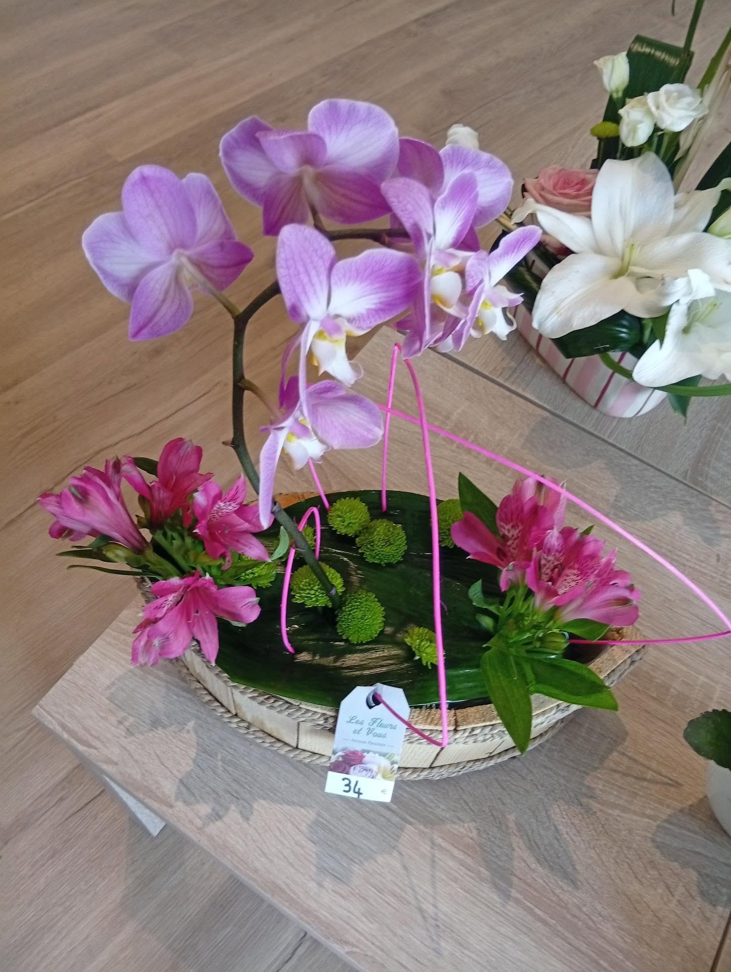 Des orchidées roses et blanches disposées dans un panier à fleurs décoratif sur une table en bois.