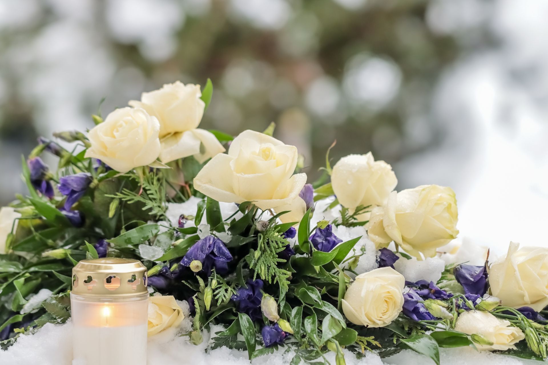 Des roses crème et des fleurs violettes disposées à côté d'une bougie allumée à l'extérieur.