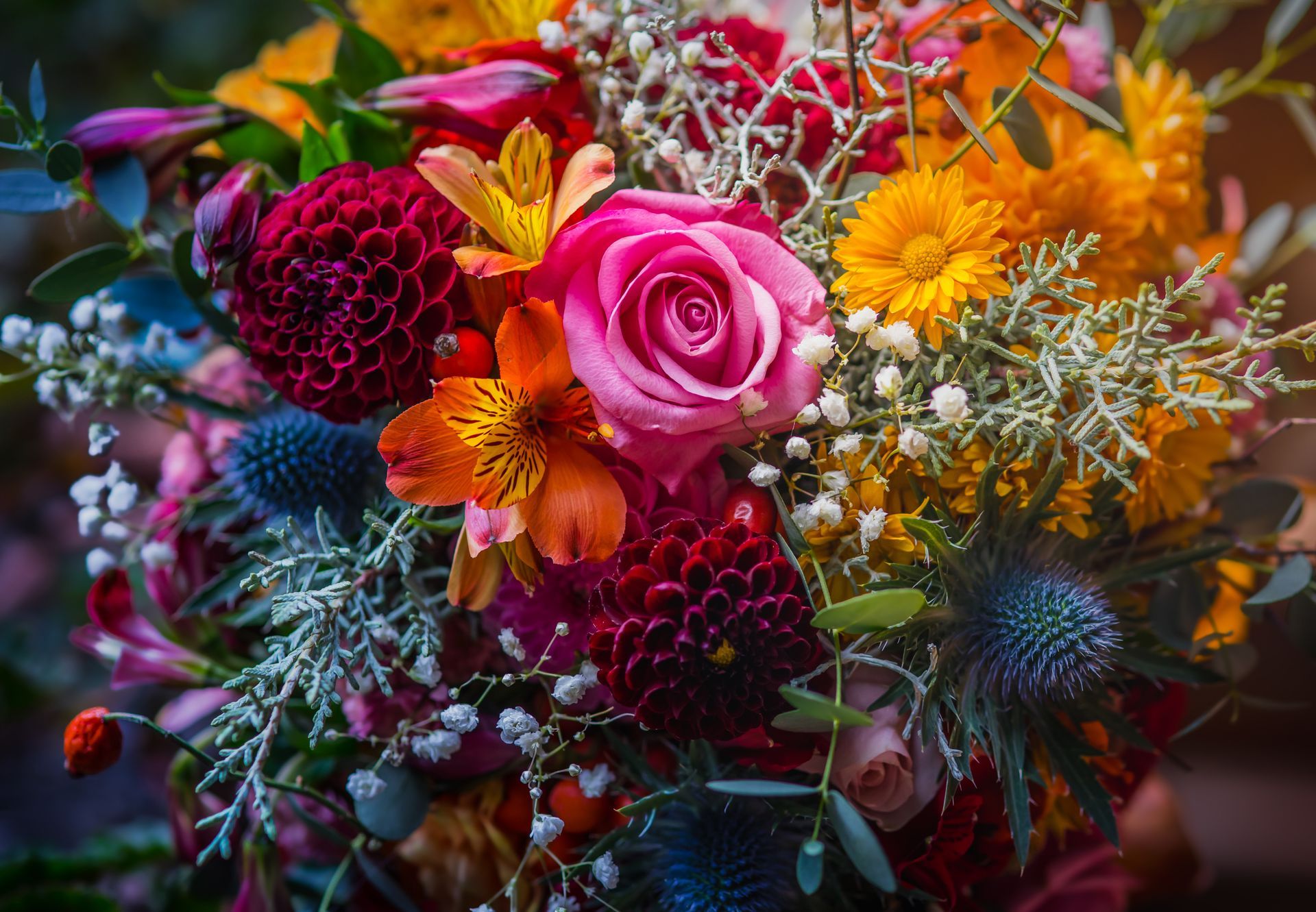 Bouquet éclatant composé de roses roses, de fleurs orange et de fleurs bordeaux foncé sur un fond légèrement flou.